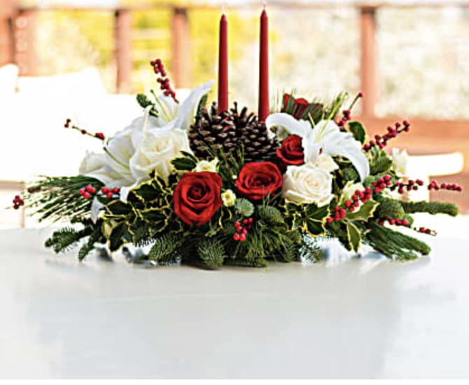 Christmas Wishes Centerpiece - Your wishes for a classic Christmas centerpiece have come true! This elegant arrangement features two glowing red taper candles atop a bed of noble fir, white pine and luxurious roses. Red and white roses are mixed with festive noble fir, white pine and variegated holly beneath two red taper candles. Red berries and pinecones add to the Christmas fun. Orientation: All-Around