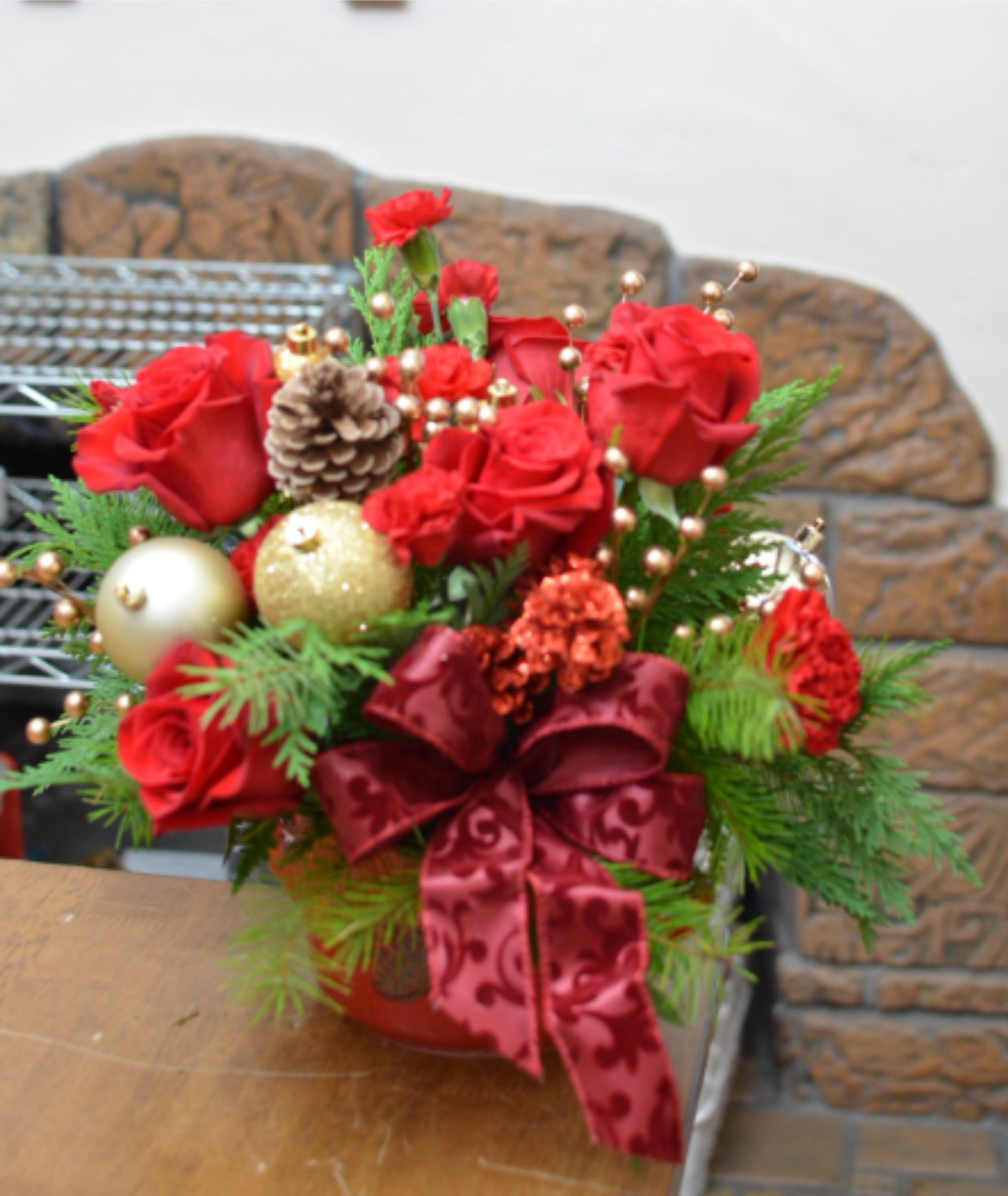 Rustic Winter Pinecone Crock - Bring the cozy charm of winter indoors with this handcrafted Rustic Winter Pinecone Crock. Designed in a deep red, crock-style container adorned with a pinecone accent, this arrangement features lush evergreen foliage, natural pinecones, and rich red accents with subtle gold details. Inspired by woodland cabins and farmhouse hearths, it’s the perfect seasonal touch for a table centerpiece, mantel, or gift. This timeless winter arrangement adds warmth, texture, and rustic elegance to any space throughout the holiday season and beyond.