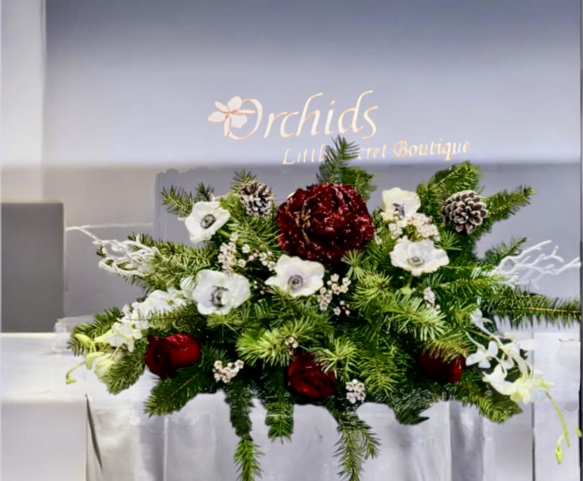 PEONIES ANEMONE ORCHIDS ROSES Luxury Christmas Centerpiece - Arrangement measures approximately 8"H x 13"W Introduce an elegant and timeless holiday centerpiece featuring burgundy peonies, winter pinecones, red roses, anemones, and white dendrobium orchids, all accented with Christmas greens. Ideal for tables or mantles to enhance the festive ambiance.