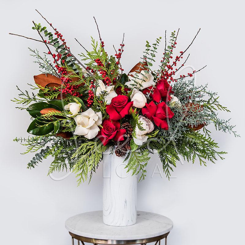 Let's Holiday - Celebrate the season in style with Let’s Holiday, a vibrant and elegant floral arrangement that captures the magic of winter. Featuring a lush mix of red and white roses, magnolia blooms, pinecones, red berries, and fragrant greenery like cedar, eucalyptus, and fir, this design brings warmth and sophistication to any space.  Presented in a marble-patterned vase, this arrangement is perfect for holiday centerpieces, seasonal décor, or festive gifting. Its rich textures and classic colors evoke cozy gatherings and joyful celebrations.