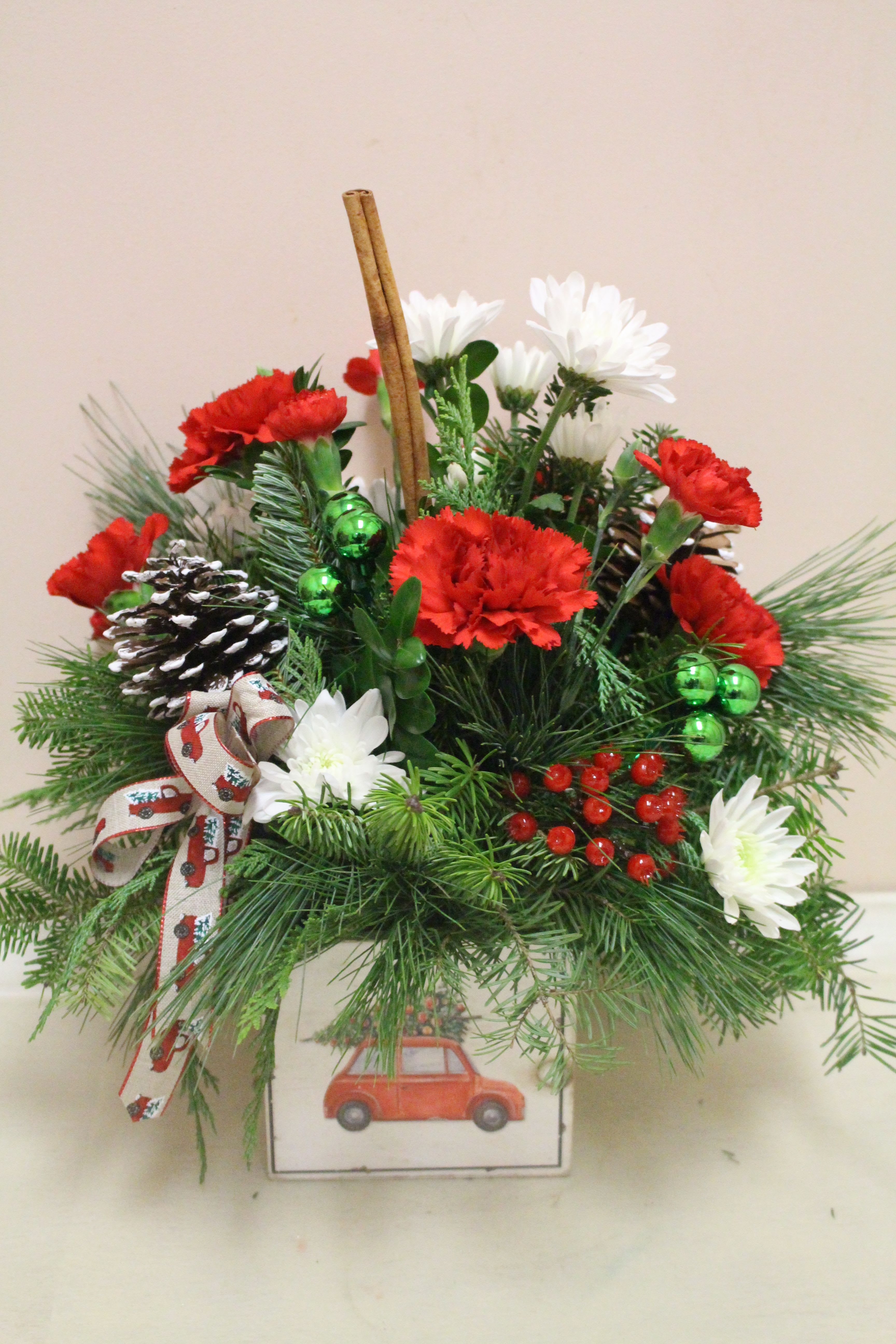 A Griswall Christmas - In a wooden box, there is a Christmas arrangement filled with winter greens and red and white flowers. The box features a car scene holding a Christmas tree.