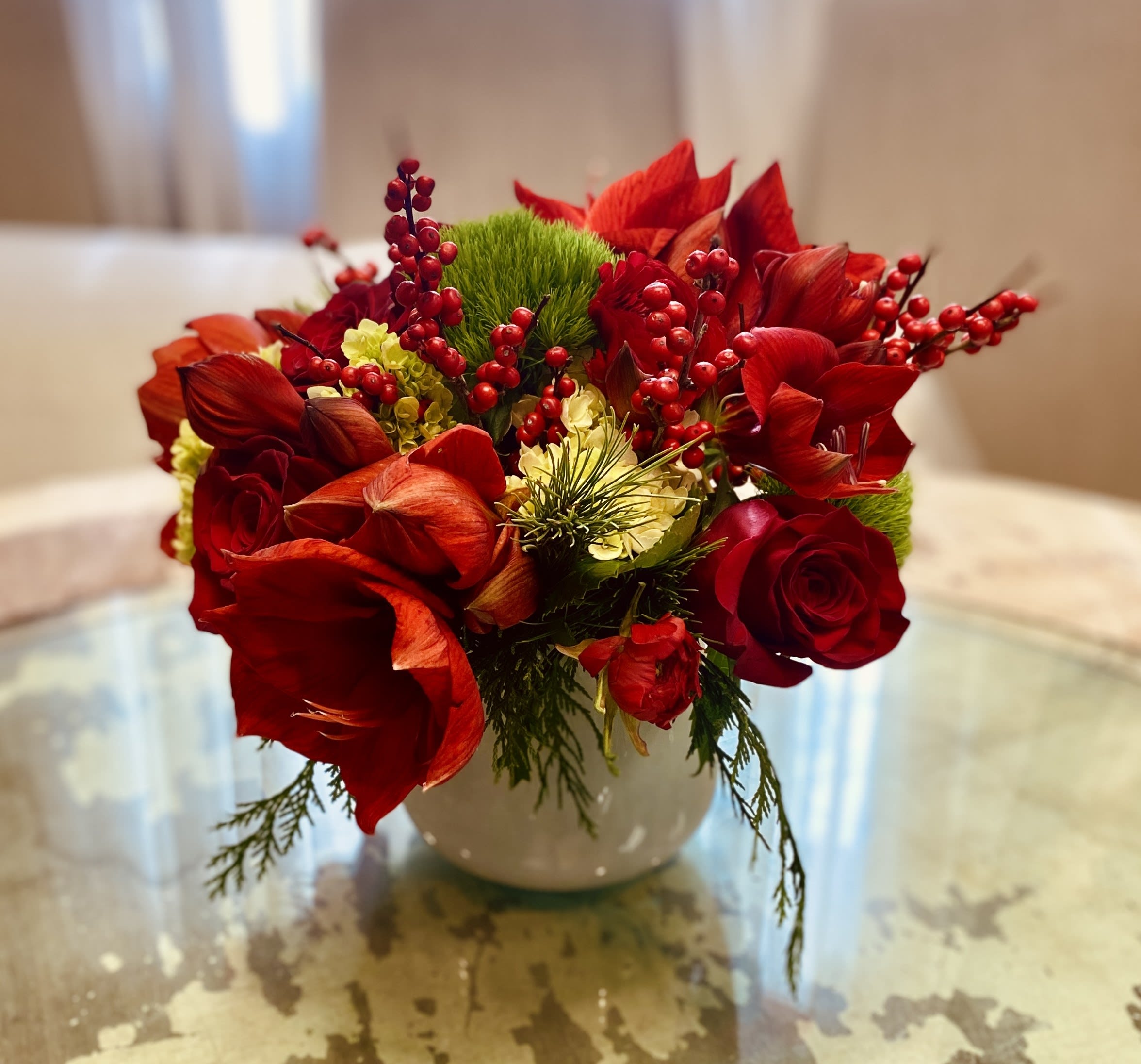 RED CHEEKS - A bright arrangement of red seasonal blooms dressed with fresh winter greens. 