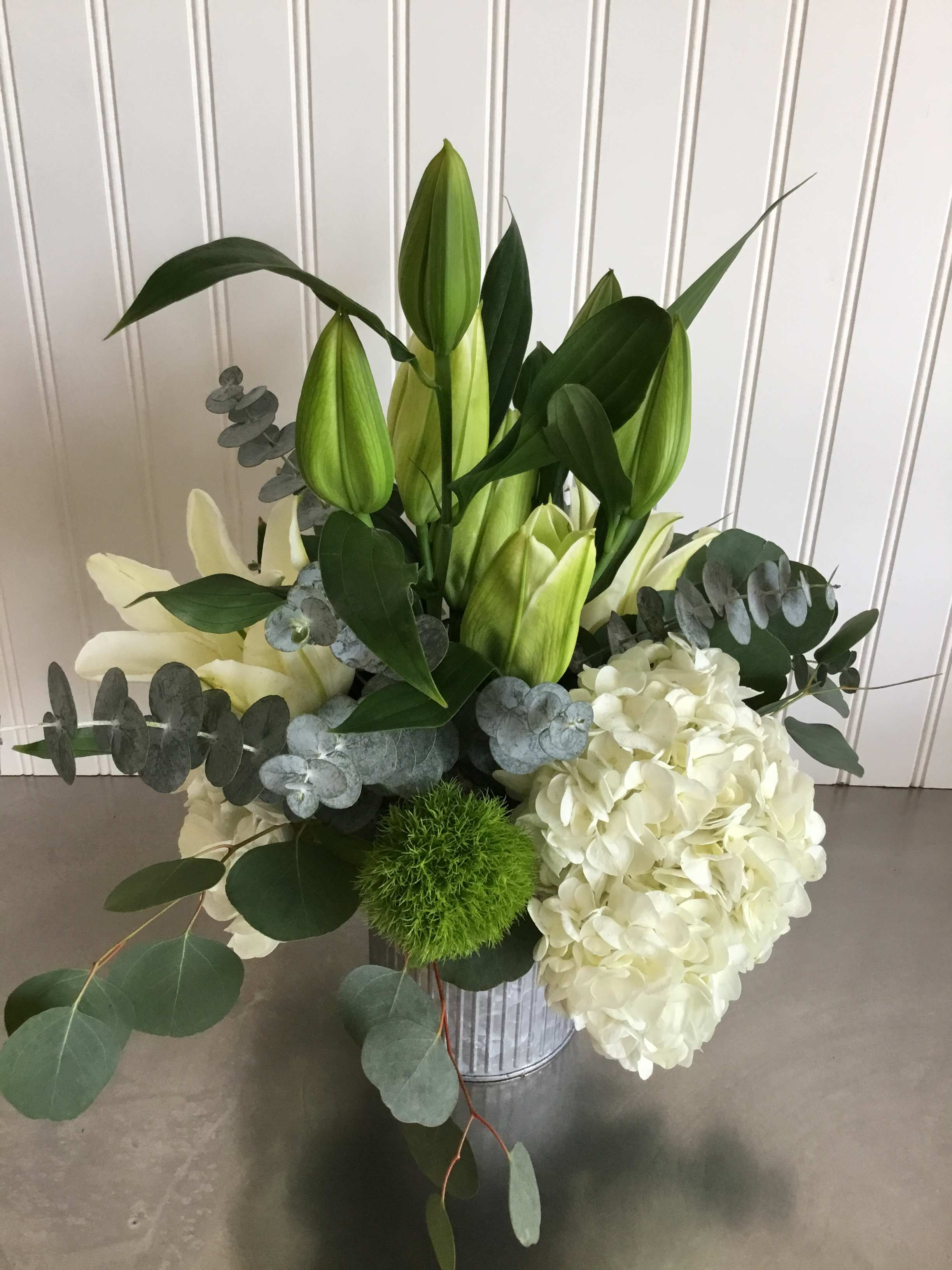 Simone - Beautiful white Hydrangea, white Lilies, Trick, and trailing Eucalyptus in a tin vase make this arrangement tres chic!