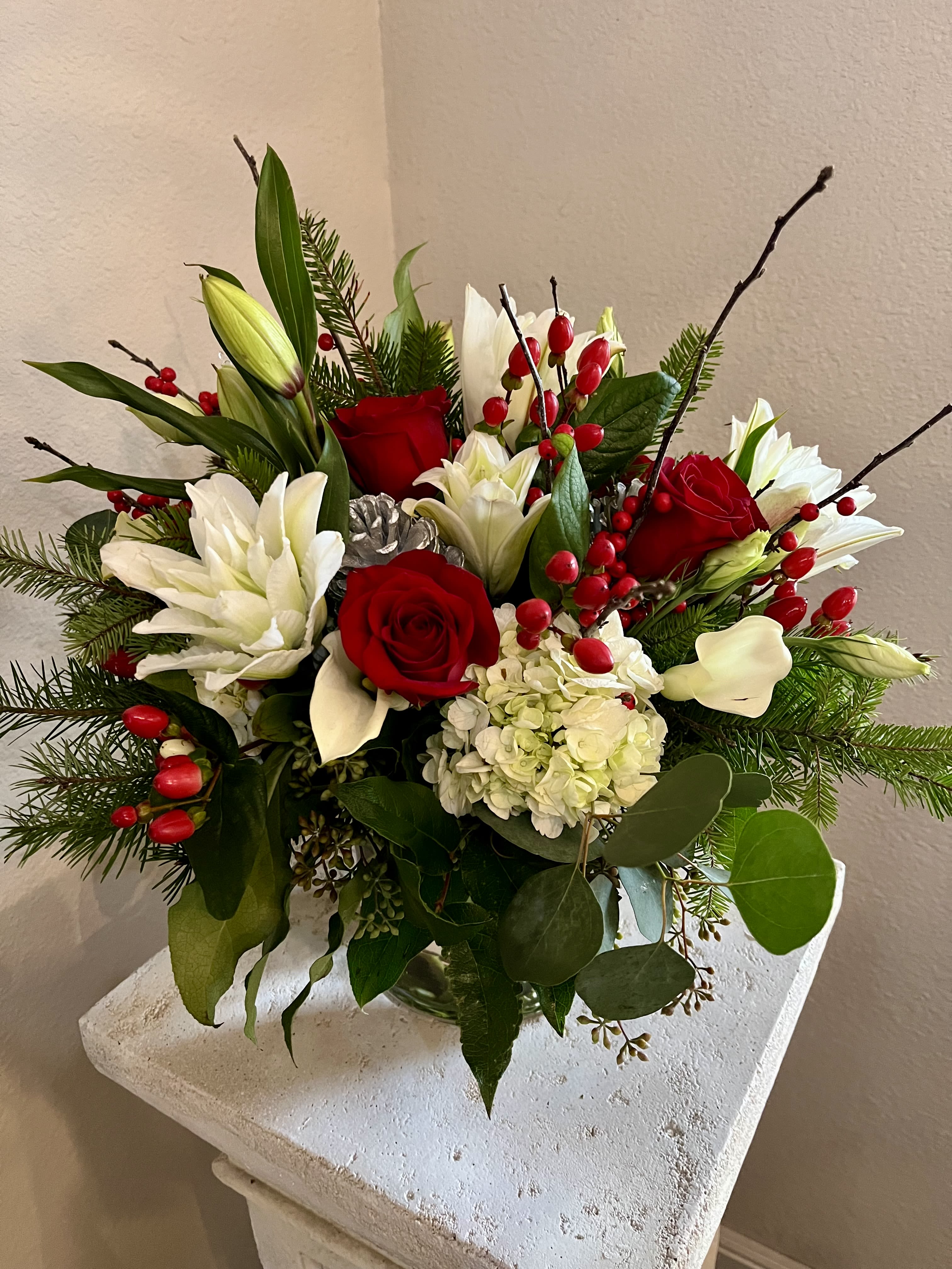 Christmas Cheer - Vase arrangement of a selection of red and white flowers accented with evergreens and berries. Individual varieties may change according to current availability. 