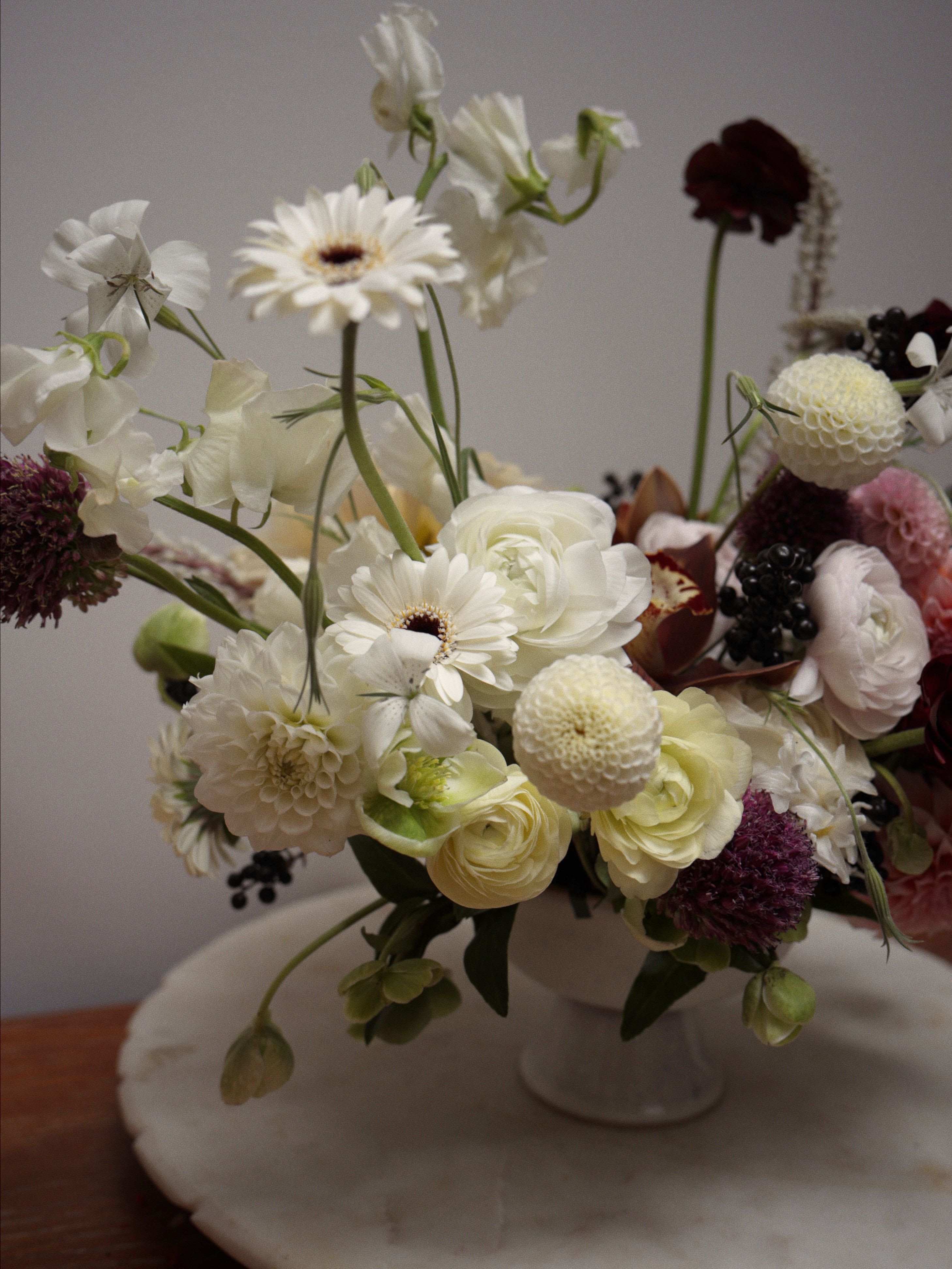 NYC mood - A refined white floral arrangement accented with deep, dark flowers for contrast. - comes in a compote styled vase.