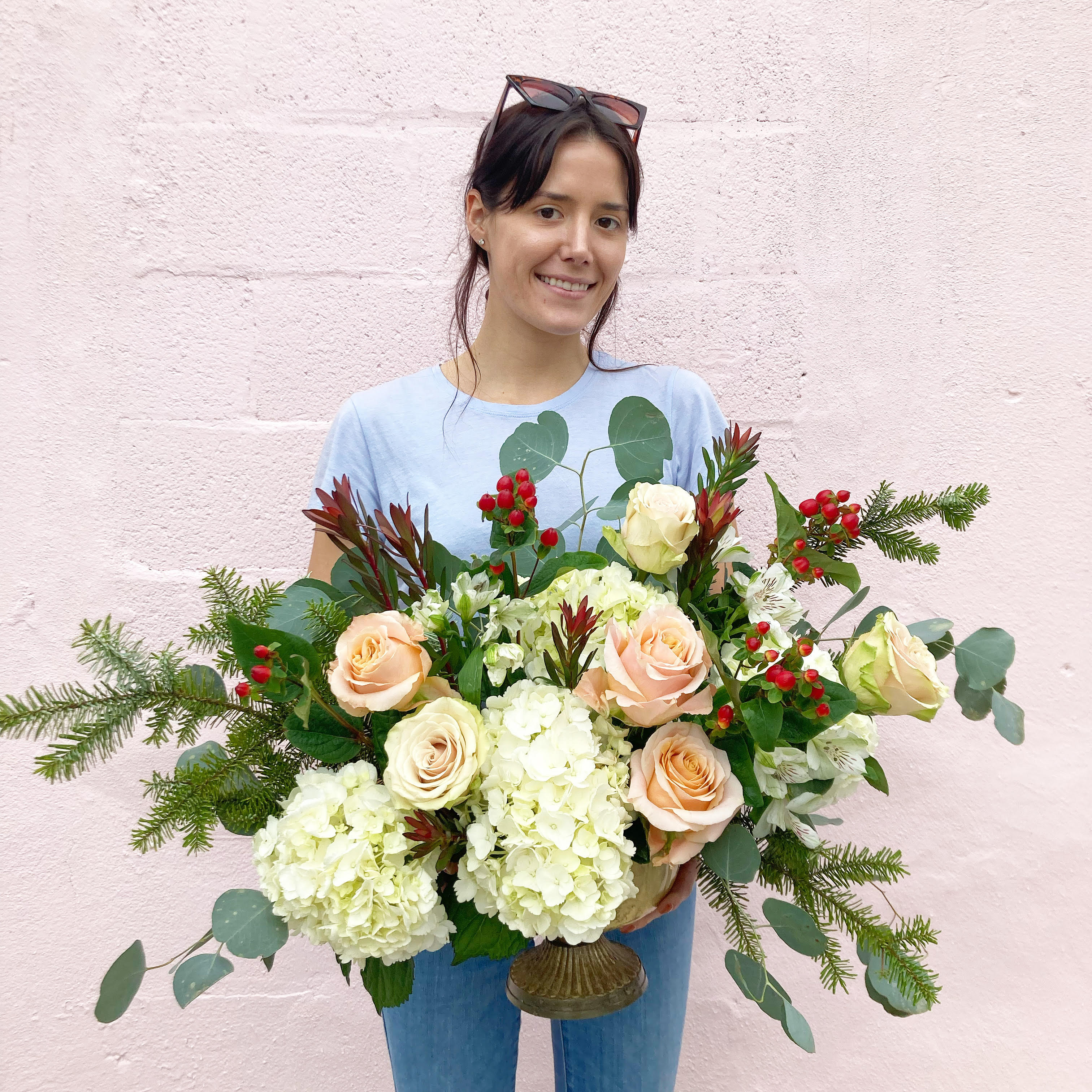 Christmas Party Centerpiece - Fluffy white hydrangeas, peach and nude garden roses, winter greens and red hypericum berries make up this lovely Christmas oblong table centerpiece perfect for your holiday entertaining in a fluted, gold metal, pedestal vase.