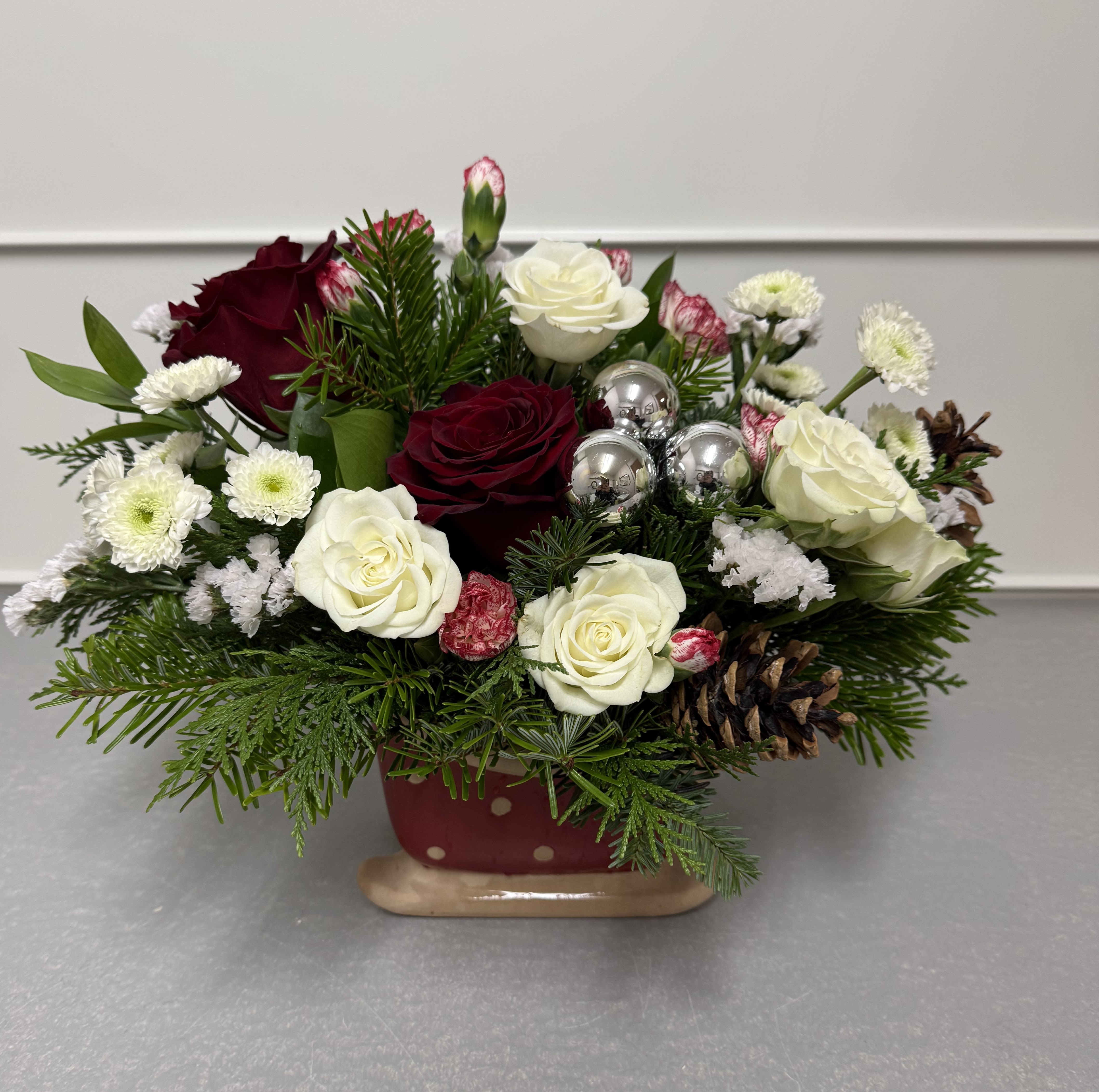Sleigh Ride - This Christmas arrangement features roses, carnations, spray roses, pinecones, and chrysanthemums with a mix of winter greens in a sleigh container. 