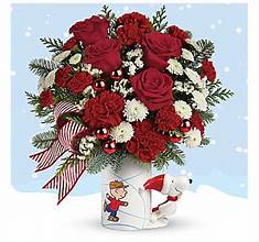 PEANUTS Christmas Mug - A delightful mix of red carnations, red miniature carnations, white button spray chrysanthemums, white sinuata statice, flat cedar, noble fir and seasonal accessories. Delivered in a PEANUTS® Christmas Mug. Approximately 13" W x 14" H