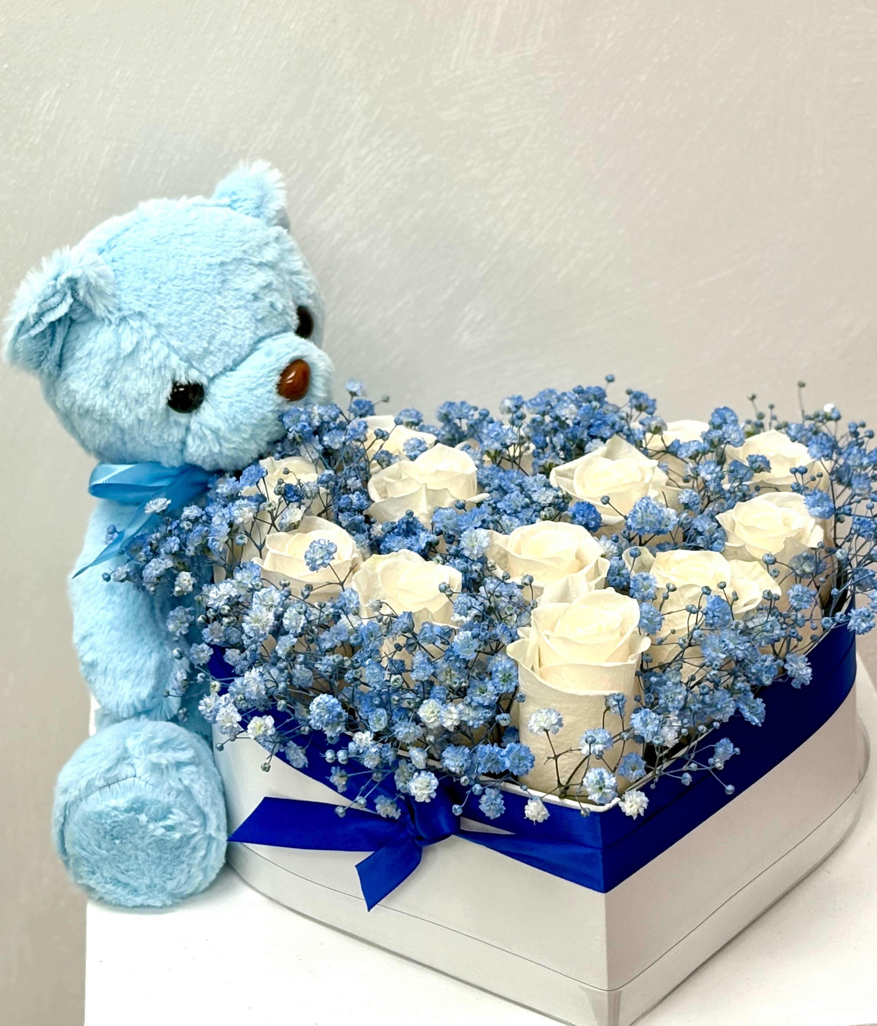 Baby Boy Bliss By VLM Flowers - A heart-shaped box filled with soft white roses and blue baby's breath, paired with a cuddly matching teddy bear—perfect for welcoming a precious baby boy.