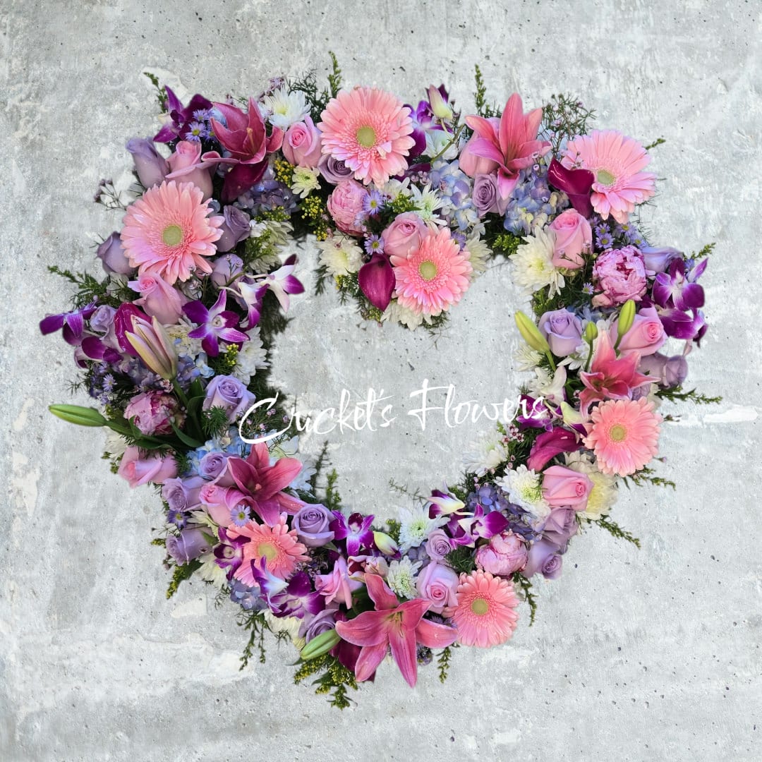 Forever in Our Hearts - This open-heart funeral design is a tender expression of love and remembrance. Crafted in a graceful heart shape, it features a soft and comforting palette of pinks, lavenders, and purples. Fresh flowers such as pink gerbera daisies, lilies, roses, orchids, hydrangea, and delicate accent blooms are thoughtfully arranged to symbolize compassion, grace, and everlasting love. Designed to honor a life deeply cherished, this heart arrangement offers a beautiful tribute for services, memorials, or celebrations of life.