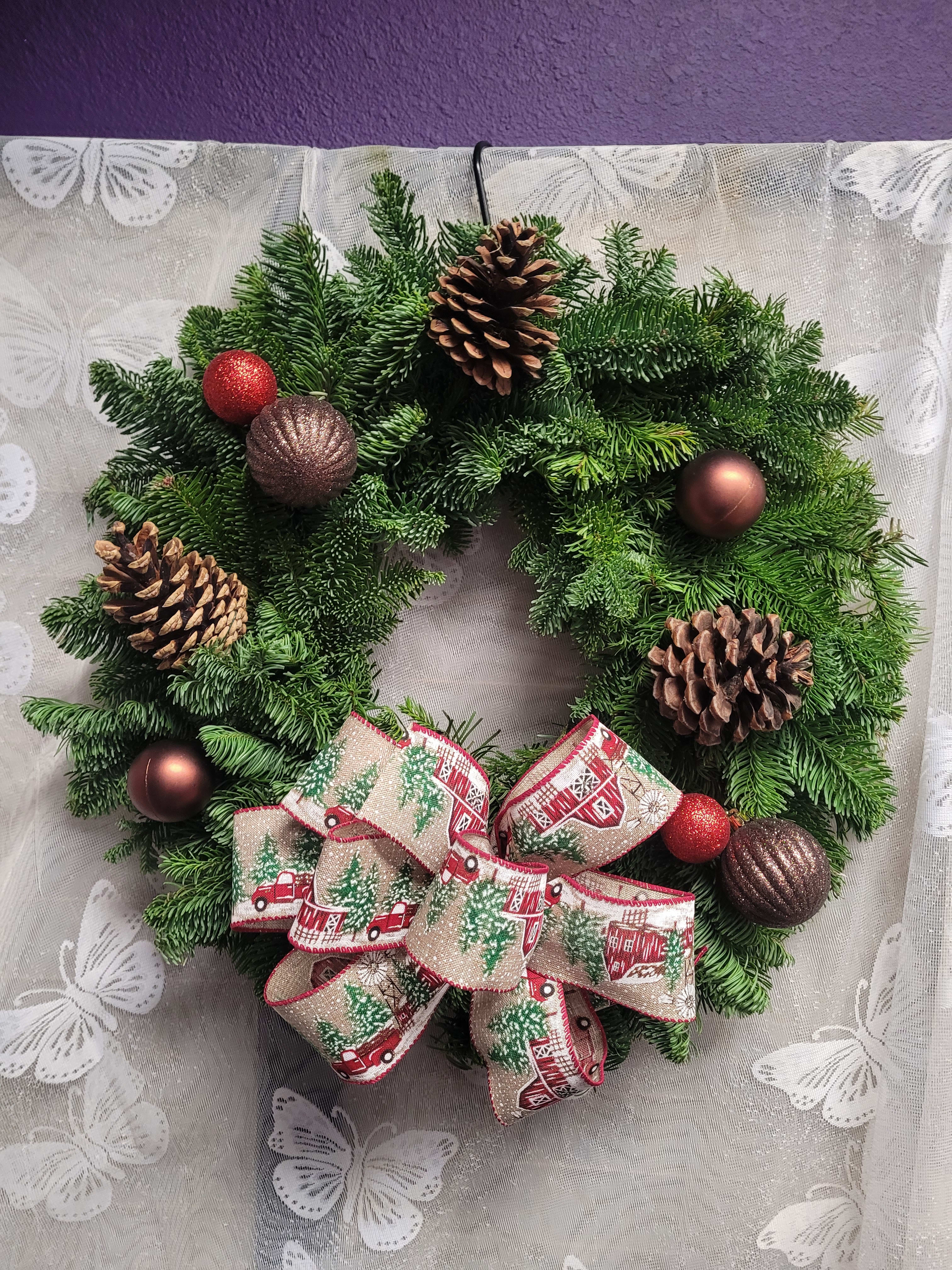 Hometown holiday wreath - Christmas wreaths, a timeless tradition that starts off the holiday season. Little red trucks and barn ribbon, red and brown balls, and natural cones decorate this fresh 20" Noble fir wreath