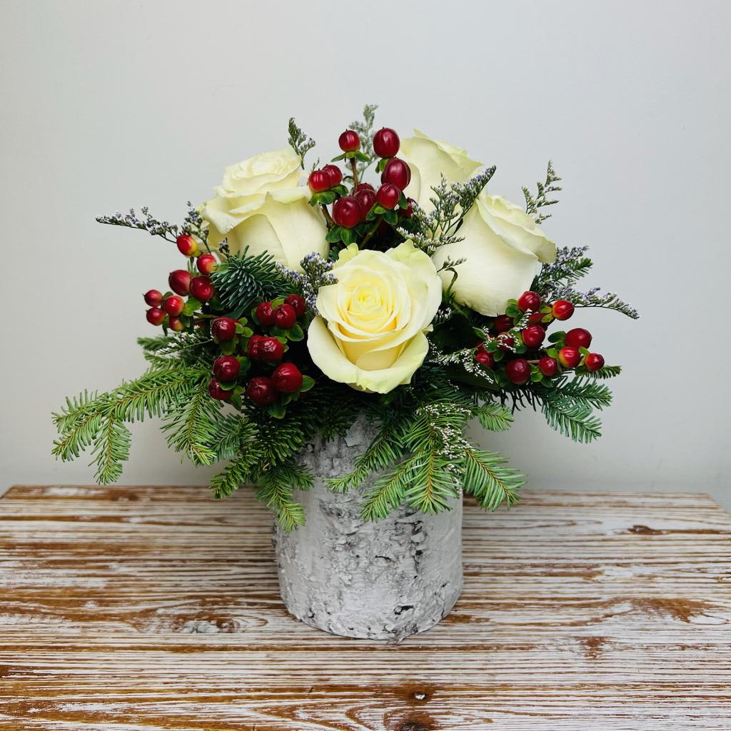 Winter Wonderland  - The feeling of winter and the holidays comes to mind with this arrangement. Beautiful white roses accented with red berries in a wooden birch cylinder container.  Approximately 12” Tall