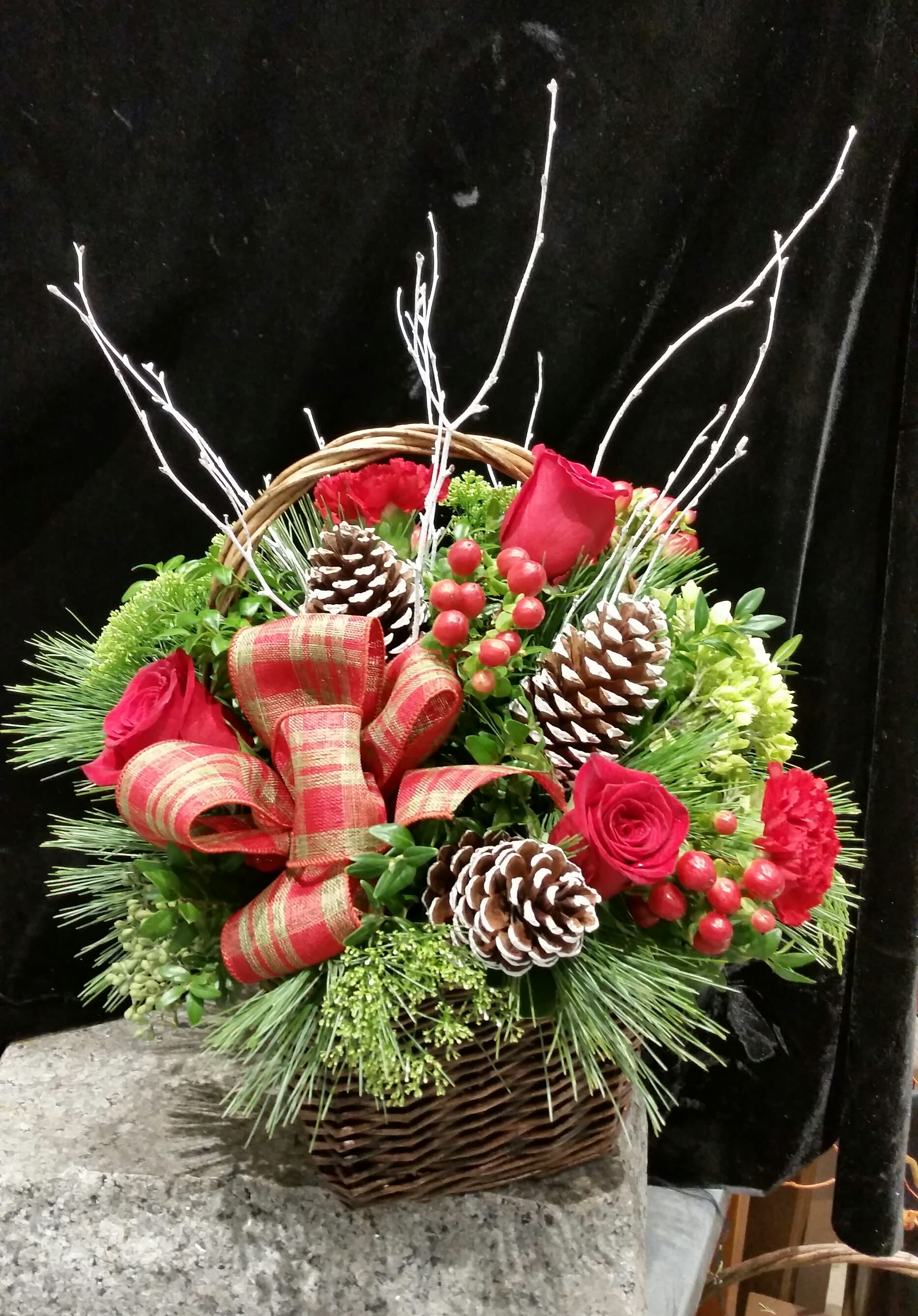Basket Full of Holiday Cheer - What could be more symbolic of a warm, joyous Christmas season with friends and family than a beautiful basket loaded with all of the season's best?  White pine, cedar and seasonal greens accent red roses and berries. Frosted pine cones, winter white branches and even a beautiful plaid bow make this basket so lovely!