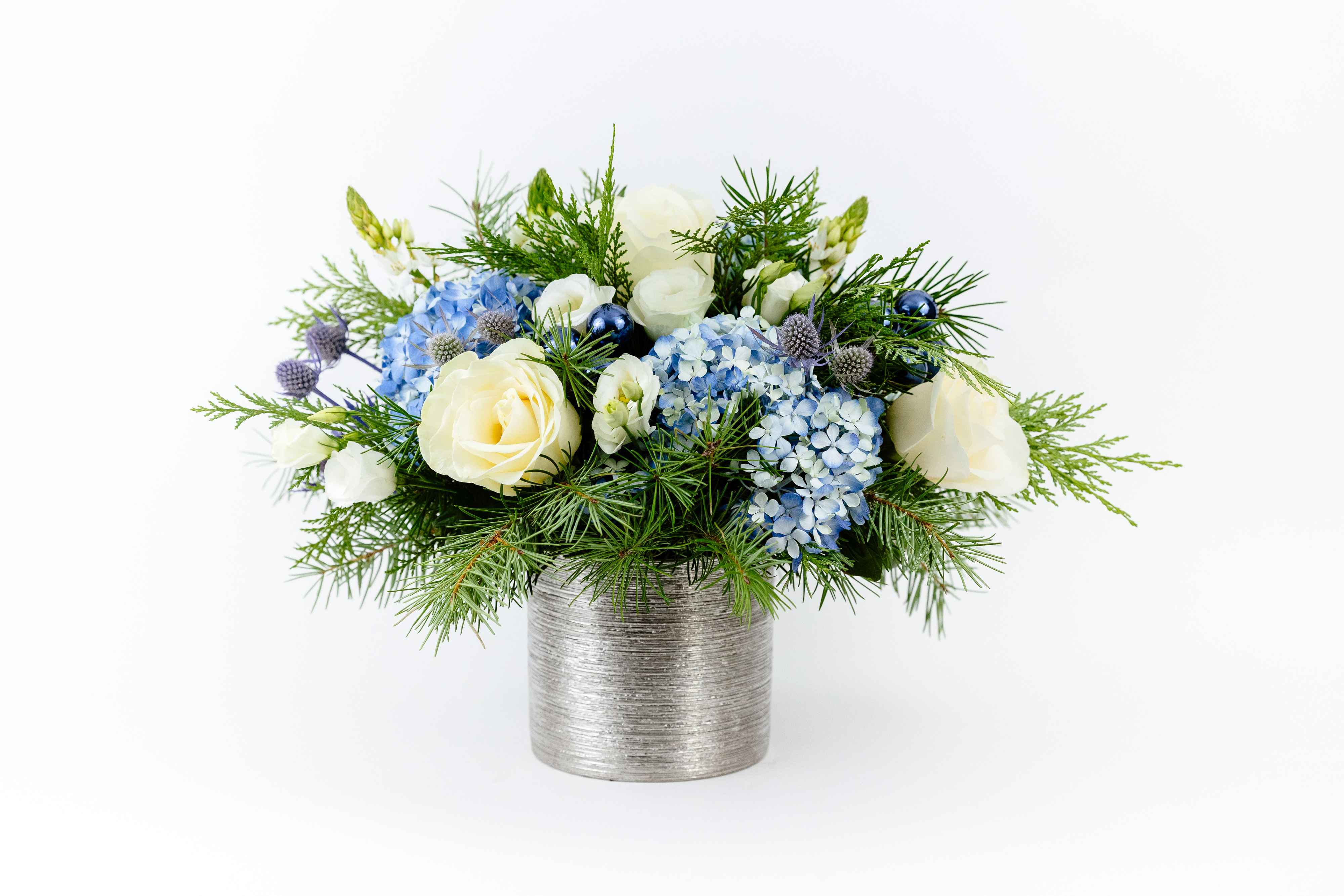 Snowy Nights  - Icy Roses and cool blue Hydrangeas will make any home ready for the winter season. Arranged in a silver container and accented with holiday greens, this arrangement is perfect for anyone looking for a snowy season here in California.  SIZE: The STANDARD flower arrangement is approximately 15” height and 15” width.  ALLERGY ADVICE: This design is low in pollen and has a moderate fragrance.  Ready to bring floral beauty into someone’s world with our autumn-inspired flower arrangement? Order this gift online now or give us a call on (415) 752-2060 if you have a question or special request.