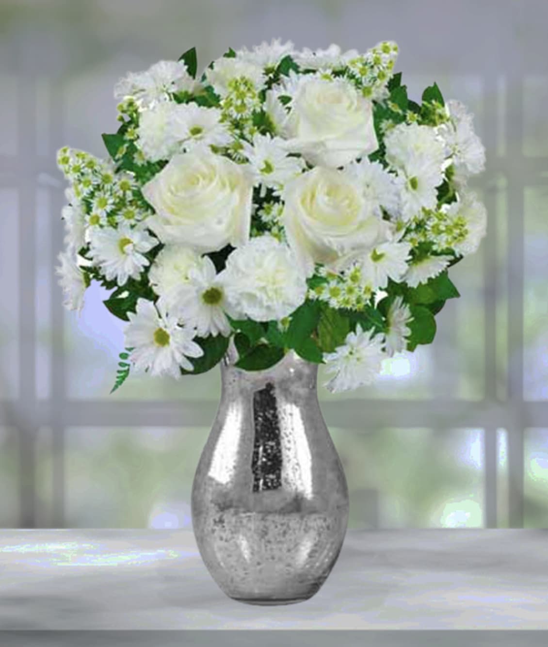 Winter Wonderland - Your recipient will be walking in a Winter Wonderland when you present them with this beautiiful arrangement. Stunning white flowers and greenery set in a silver vase, it boasts a timeless, simplistic elegance, adding a touch of Winter to any room it's displayed in.  Item pictured is a depiction of an arrangement that we will make as similar as possible with the same look and feel. 