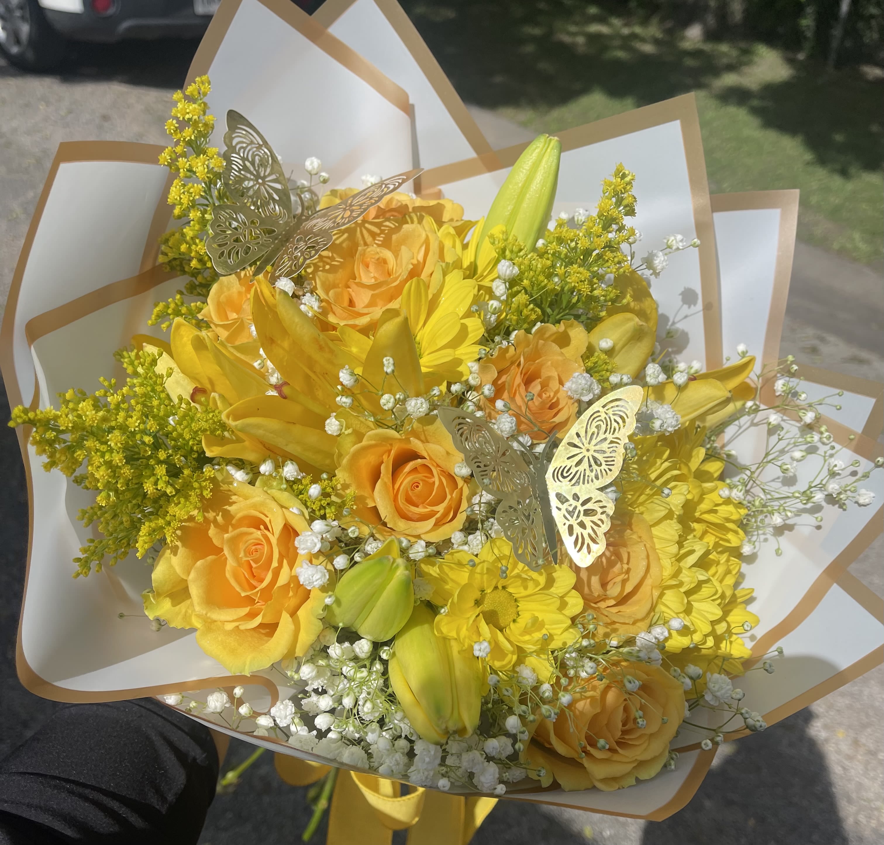 Yellow Fields Wrapped Bouquet - Yellow roses, lillie's, daisies, baby's breath, and  Solidago wrapped in white paper.    In some instances, our photo may represent an overall theme or look and include a one-of-a-kind vase which cannot be exactly replicated.  Although the actual bouquet may not precisely match the photo, its temperament will. Occasionally, substitutions of flowers and/or containers happen due to weather, seasonality and market conditions which may affect availability. If this is the case with the gift you’ve selected, we will ensure that the style, theme and color scheme of your arrangement is preserved and will only substitute items of equal value or higher value.  If any design elements are of major importance to your order, please include them in the florist instructions at checkout or contact us to ensure availability.