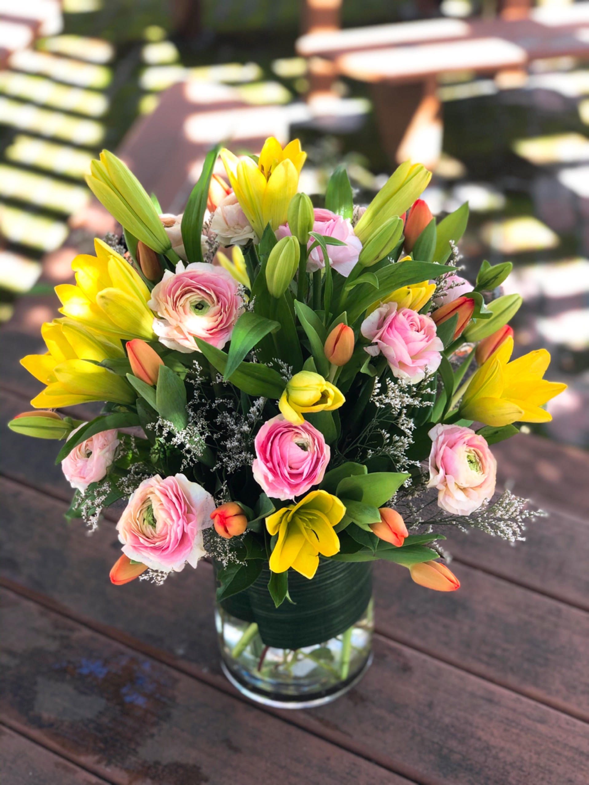 Spring Bouquet - - 3 Stems Yellow Lilies - 10 Stem Pink Ranunculus - 10 Stems Orange Tulips - White Fillers - Greenery - 6 x 8 Inches Cylinder Clear Vase