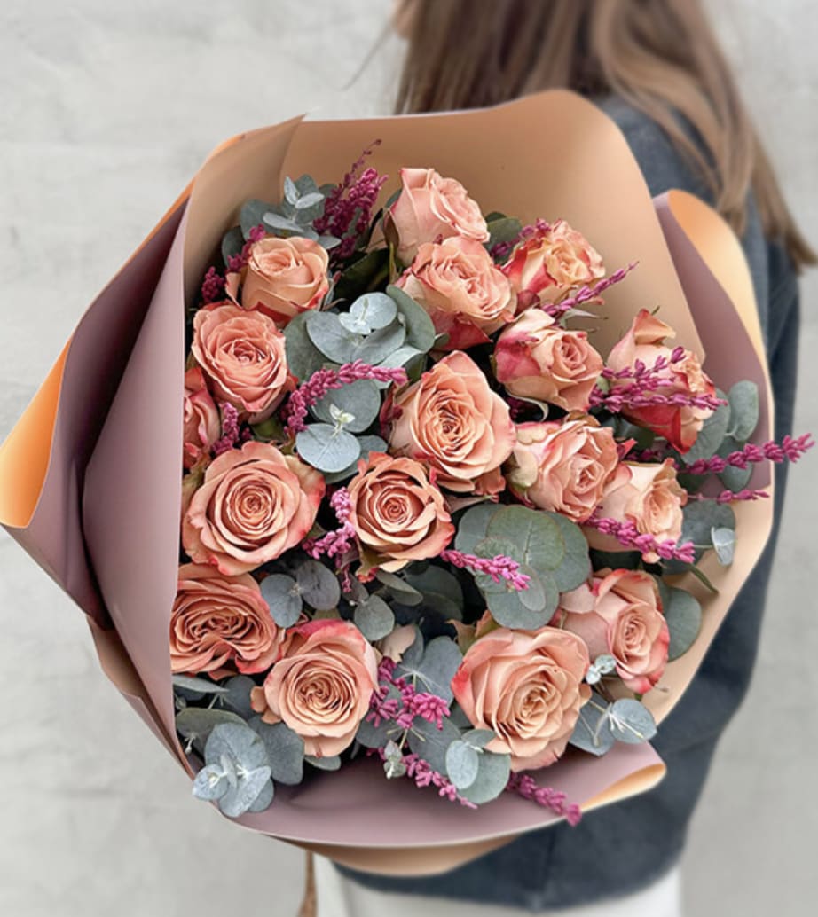 Sunset Whisper - A radiant bouquet of peach-hued roses with accents that captures the gentle glow of the setting sun wrapped in decorative paper and ribbon.