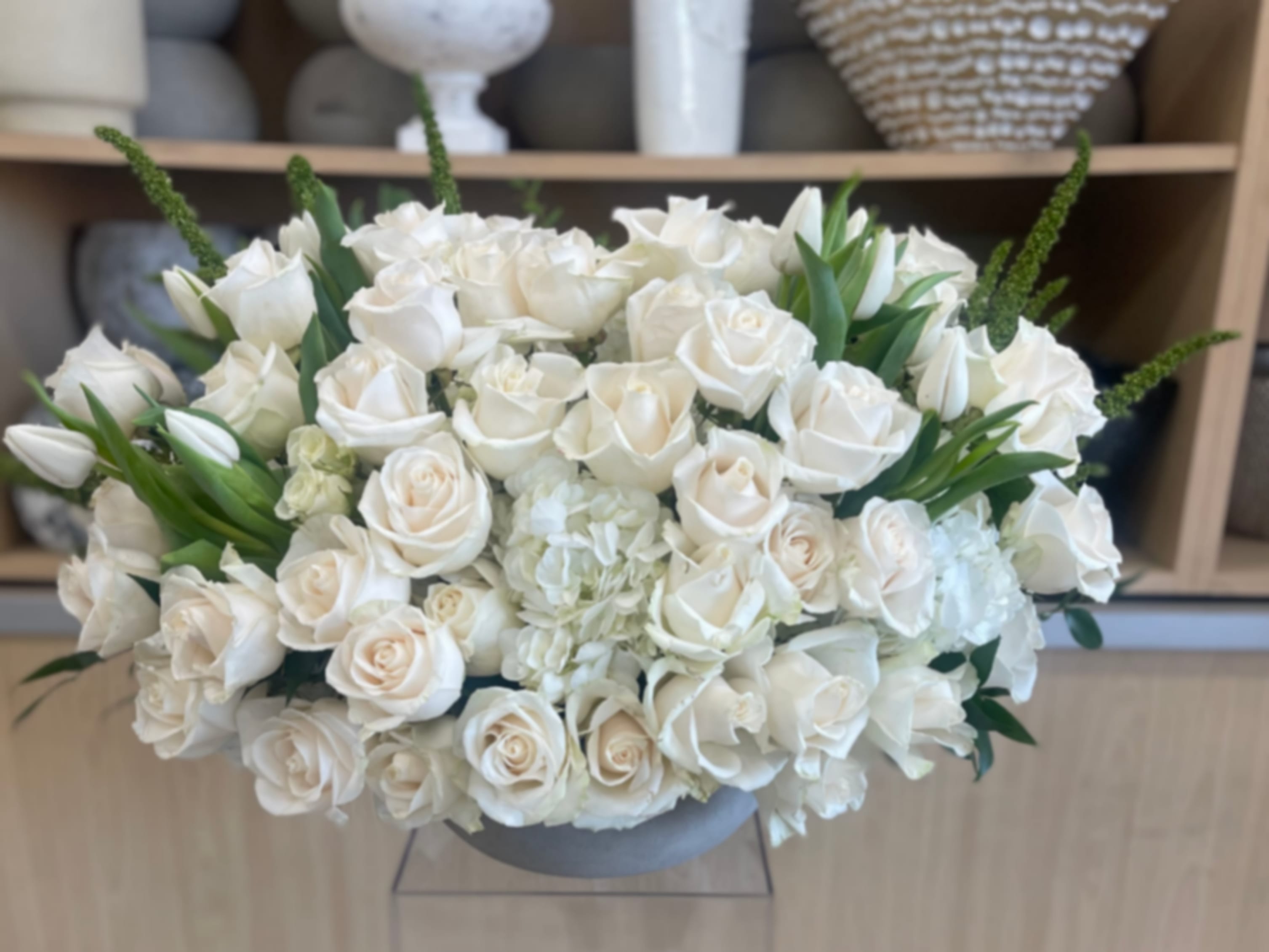 Winter White Rose Centerpiece - A timeless winter centerpiece made with fresh cut flowers, featuring an abundant arrangement of premium white roses, white hydrangea, and seasonal greenery. Designed low and full in a modern gray ceramic bowl, this arrangement offers an elegant holiday look perfect for winter celebrations, formal tables, and refined gifting.  Hand-designed and delivered fully arranged and gift-ready.  Note: Exact flowers may vary slightly based on seasonal availability while maintaining overall color palette, size, and style.