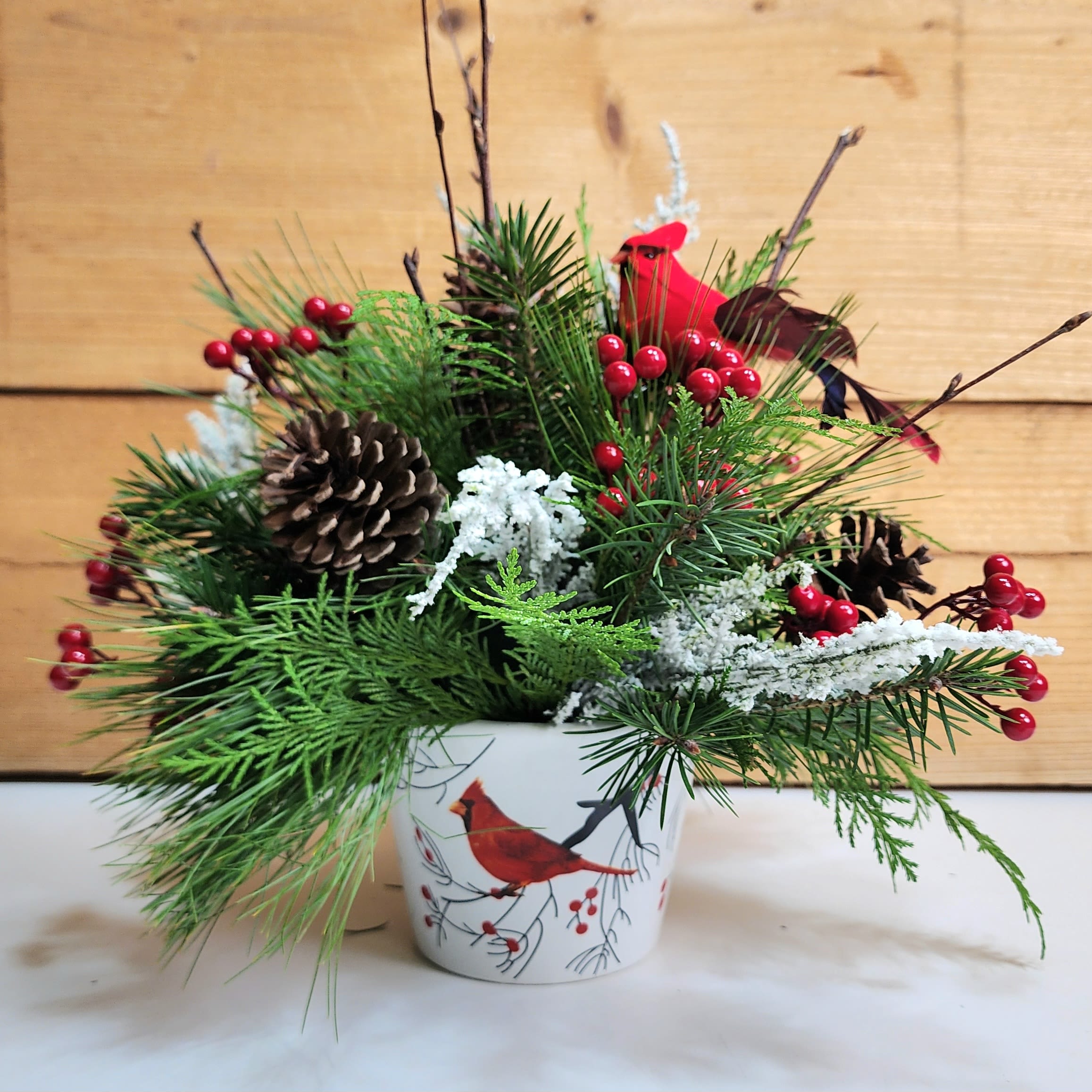 Cardinal Christmas - Cardinal Christmas is a delightful arrangement for the winter season, with a mix of winter greens along with wintery decorative accents including a cardinal pick, natural pinecones, birch branches, and faux berries and frosted branches. This arrangement is presented in a lovely container featuring a cardinal sitting on a branch. Cardinal Christmas is perfect for any time during the winter months, whether it's specifically for a holiday, or just because!   Dimensions approx. L 12" x H 15"