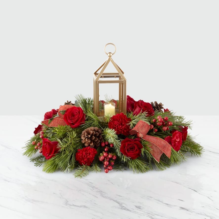 I'll Be Home Lantern Centerpiece - Bring your guests together with an elegant centerpiece worth gathering around. A stunning collection of roses, hypericum berries, carnations and greens sit around a lantern with a festive ribbon accent. Our I'll Be Home Centerpiece helps light up every celebration this season. *Note: While the ribbon  and lantern color in your arrangement may change due to availability, we can promise the centerpiece will be fresh, bright and perfect for the holidays.