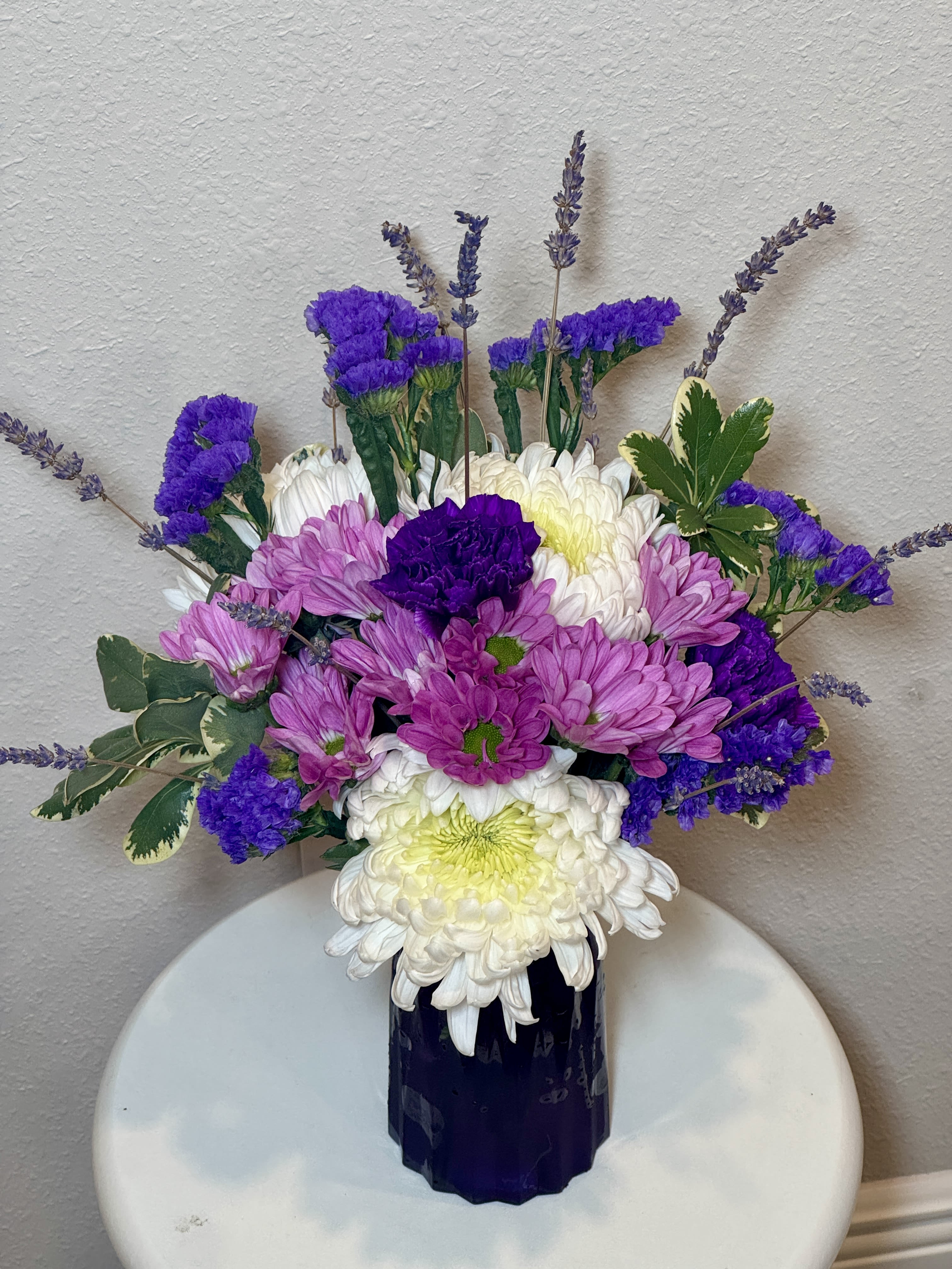 Serenity Bliss blush  - Serenity Blooms arrangement combines the gentle beauty of purple mums, carnations, and classic white daisies. This fresh mix creates a peaceful and uplifting display, perfect for birthdays, get-well wishes, or simply letting someone know you care. 