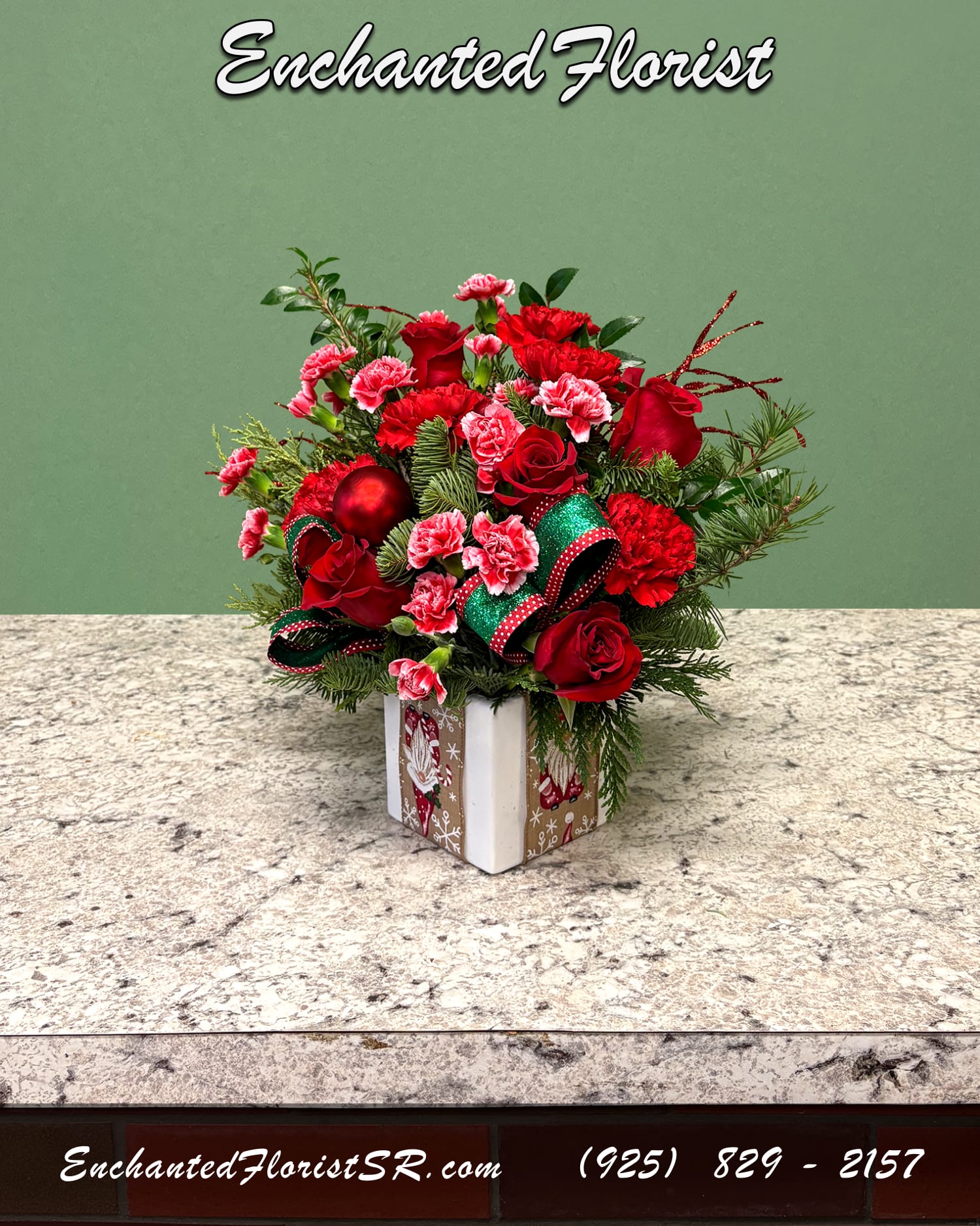 Blooming Giftbox - Holiday Arrangement - A festive holiday arrangement designed to feel like a beautifully wrapped gift. Showcasing a red Christmas palette, featuring flowers such as roses, carnations, and mini carnations. Accented with fresh noble fir, leather fern, and shiny red ornaments for a classic seasonal touch. Presented in a white ceramic cube that mimics the charm of a holiday gift box.   Perfect for spreading joy, brightening celebrations, or surprising someone special with a little wrapped-up holiday cheer.  Orientation: One-Sided  Arrives In: White ceramic cube vase  Approximate Dimensions: 12" Tall 10" Wide 4" Vase Diameter