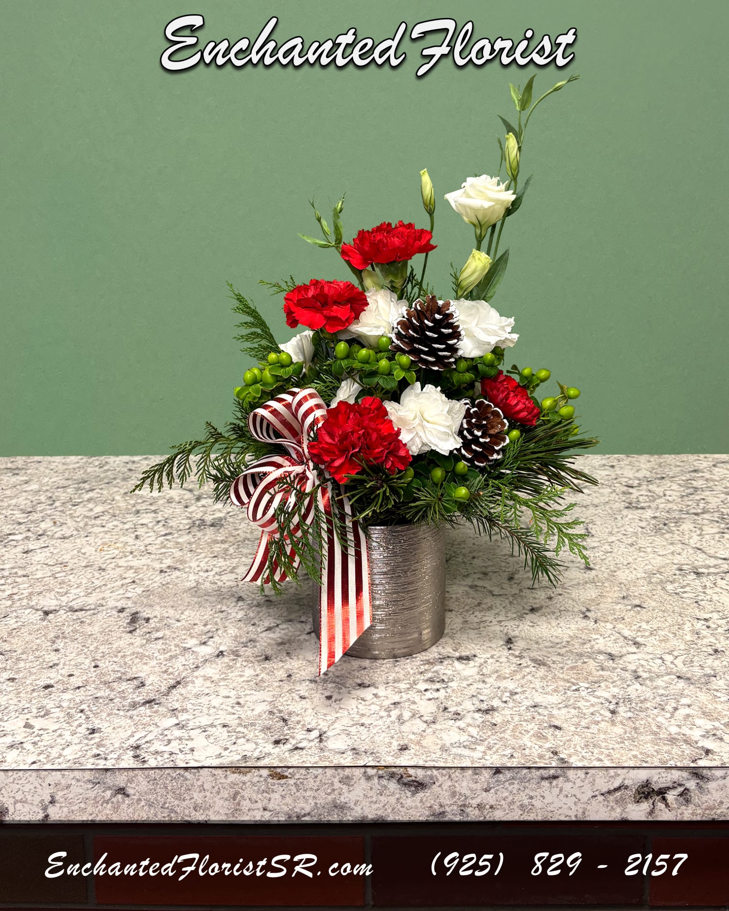 Charmed - Holiday Arrangement - A cheerful holiday arrangement showcasing a festive red, white, and green palette. Featuring flowers such as roses, lisianthus, and carnations. Accented with hypericum berries, freshly-cut fir, and decorative snowy acorns. Presented in an elegant silver cylinder.   Arrives In: Cylindrical silver ceramic vase  Orientation: All-Around  Approximate Dimensions: Height: 14" Width: 8" Vase Diameter: 3"