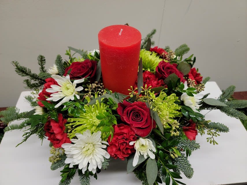 Red Pillar Candle Centerpiece - Modern Pillar candle centerpiece made with an assortment of evergreens, red roses, red carnations, white cushions and green mums accented with seeded eucalyptus.