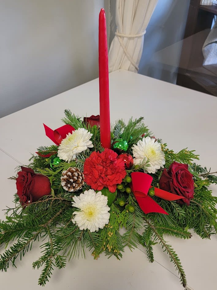 "Joy" Traditional Candle Centerpiece - Send Joy with the single candle centerpiece! An assortment of fragrant evergreens arranged with red carnations, red roses, white mums, berries, pine cones and red ribbons. Standard size is shown. Deluxe and premium include more flowers and greens. 