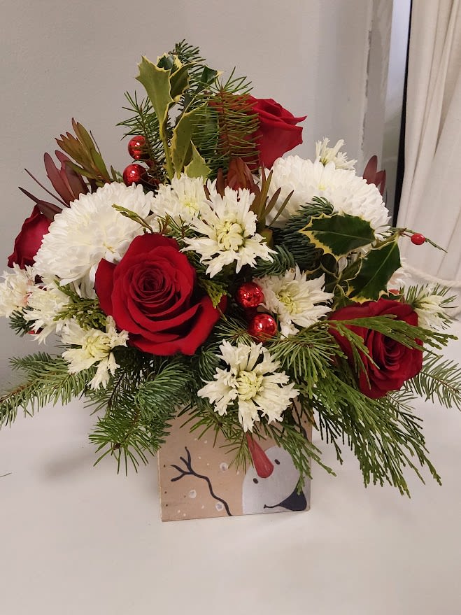 Happy Snowman  - Cheerful wooden cube decorated with a happy snowman sending holiday greetings.  Flowers include red roses, white mums, safari sunset, mixed winter greens and red christmas balls. Standard is shown, Deluxe and Premium sizes include additional flowers and the arrangement increases in size.  The wooden box is 5x5 and the standard size arrangement is estimated 12x12.
