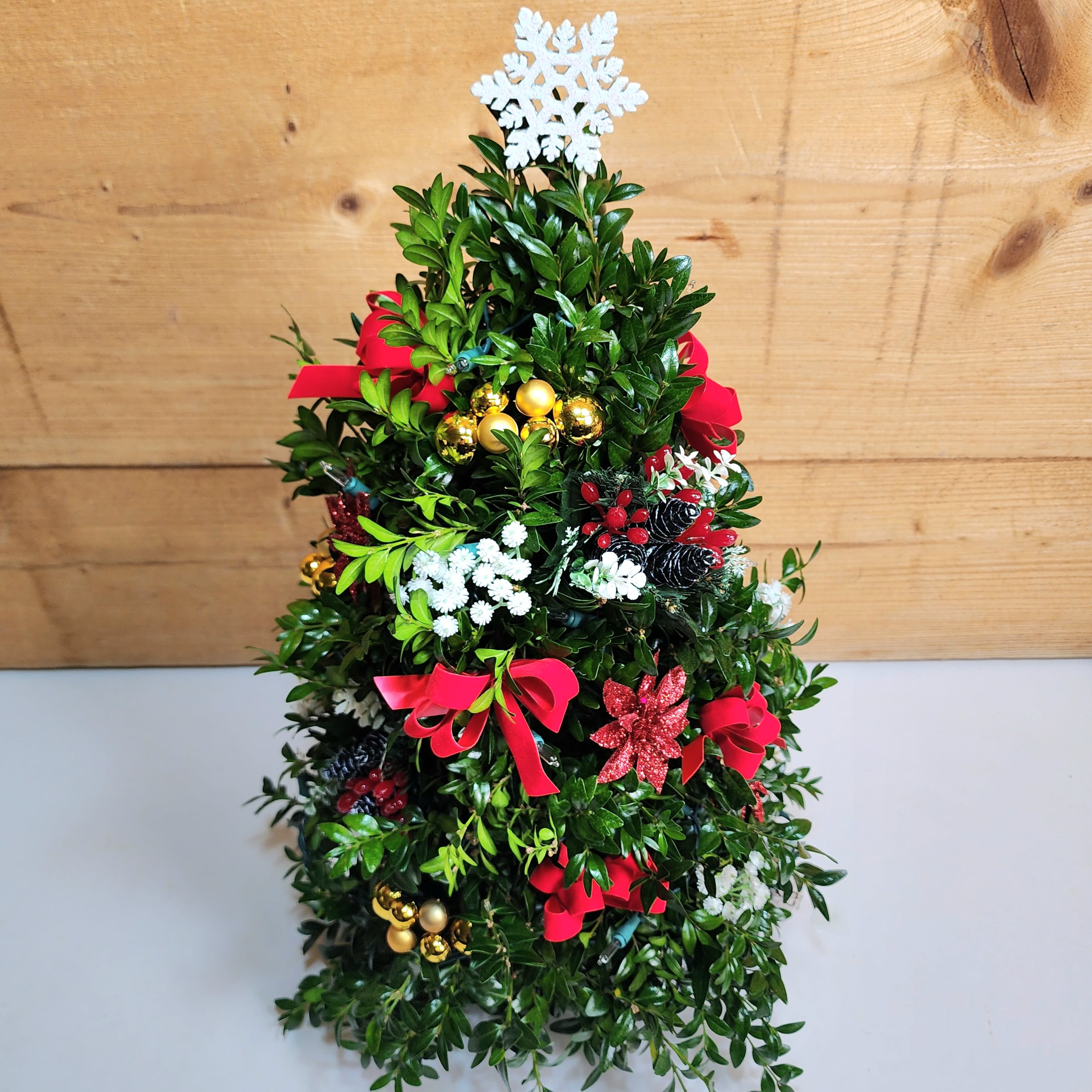 Medium 20" Boxwood Tree - Medium Boxwood Tree 20 inch with lights and decorations featuring elegant boxwood stems that are hand arranged to look like a mini Christmas tree, complete with all the festive trimmings.  Decorations may vary.  Our boxwood trees are made using a floral foam base.  If recipient adds water to the top of the tree to saturate the foam, it should last through the holiday season. 