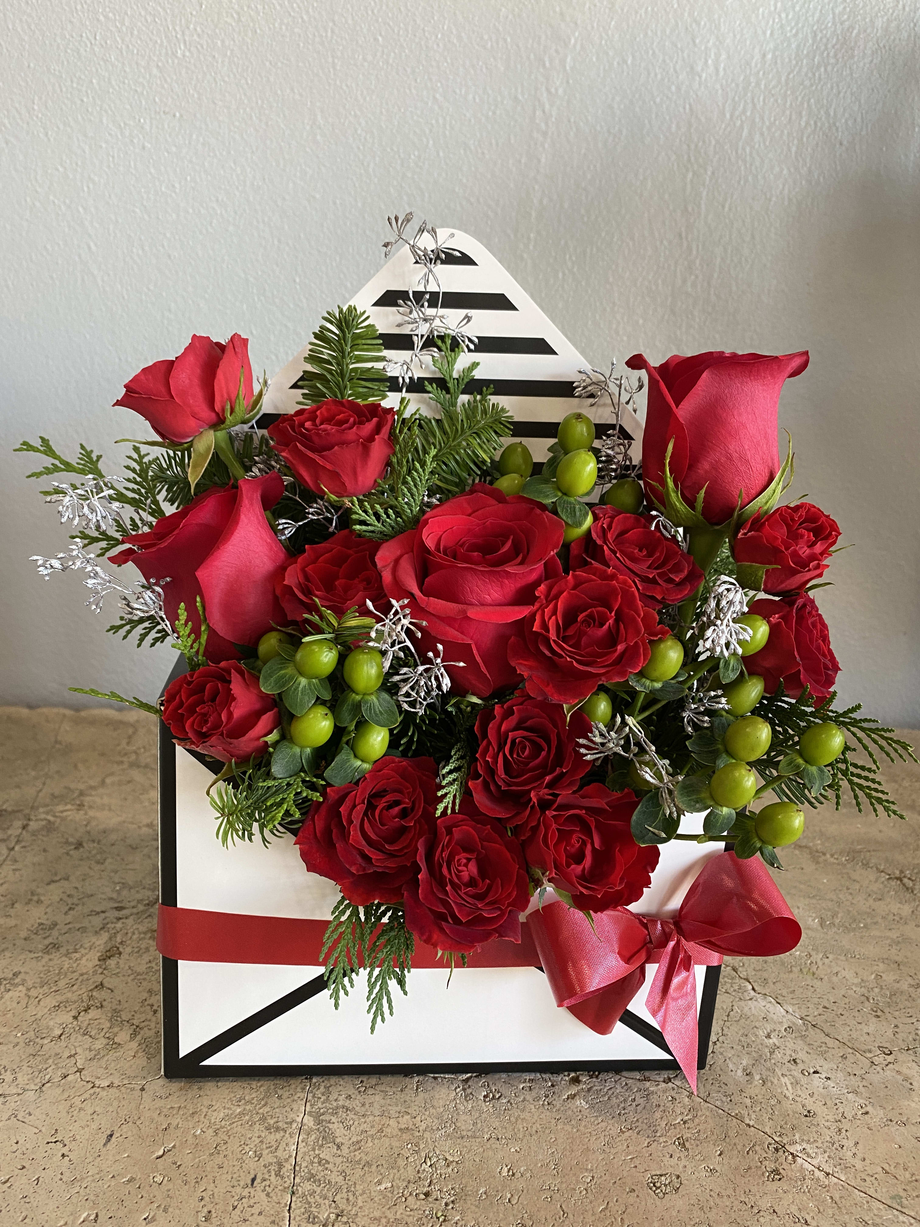 Merry Christmas Box - Envelope Box full of fresh red roses large and small, accented with green hypericum berries and Christmas greens. Box is decorated with a lovely red ribbon tie. For anyone who appreciates something different. Color of box might be different from one shown. 