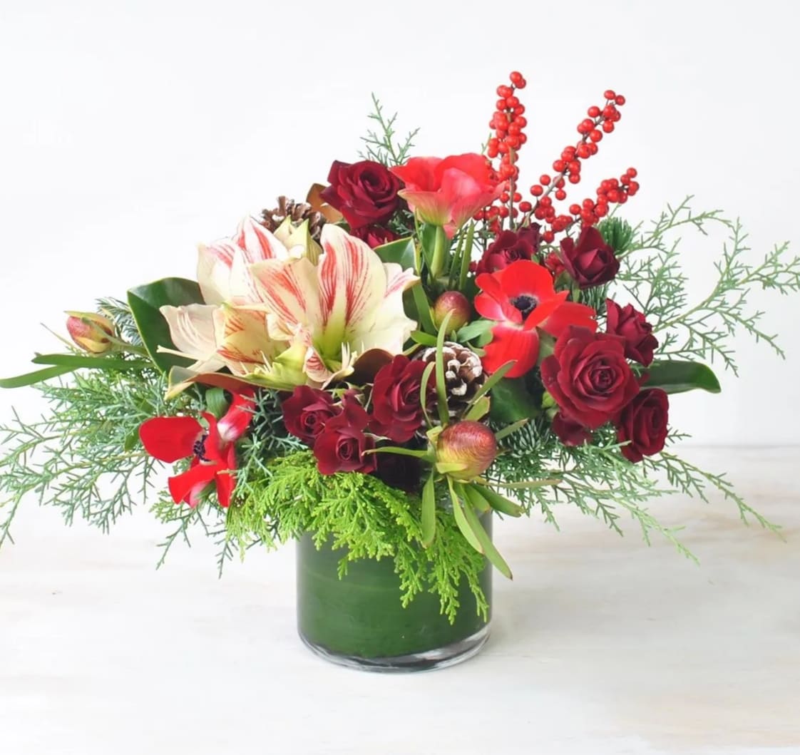 Crimson Festivity - This timeless Christmas ensemble captivates with its vibrant reds and lively greens, thoughtfully arranged with gorgeous Amaryllis flowers, crimson red sweetheart roses, ilex berries, complemented by the aromatic evergreens. This arrangement embodies the cheerful holiday atmosphere, inviting joy and merriment into any space it graces.