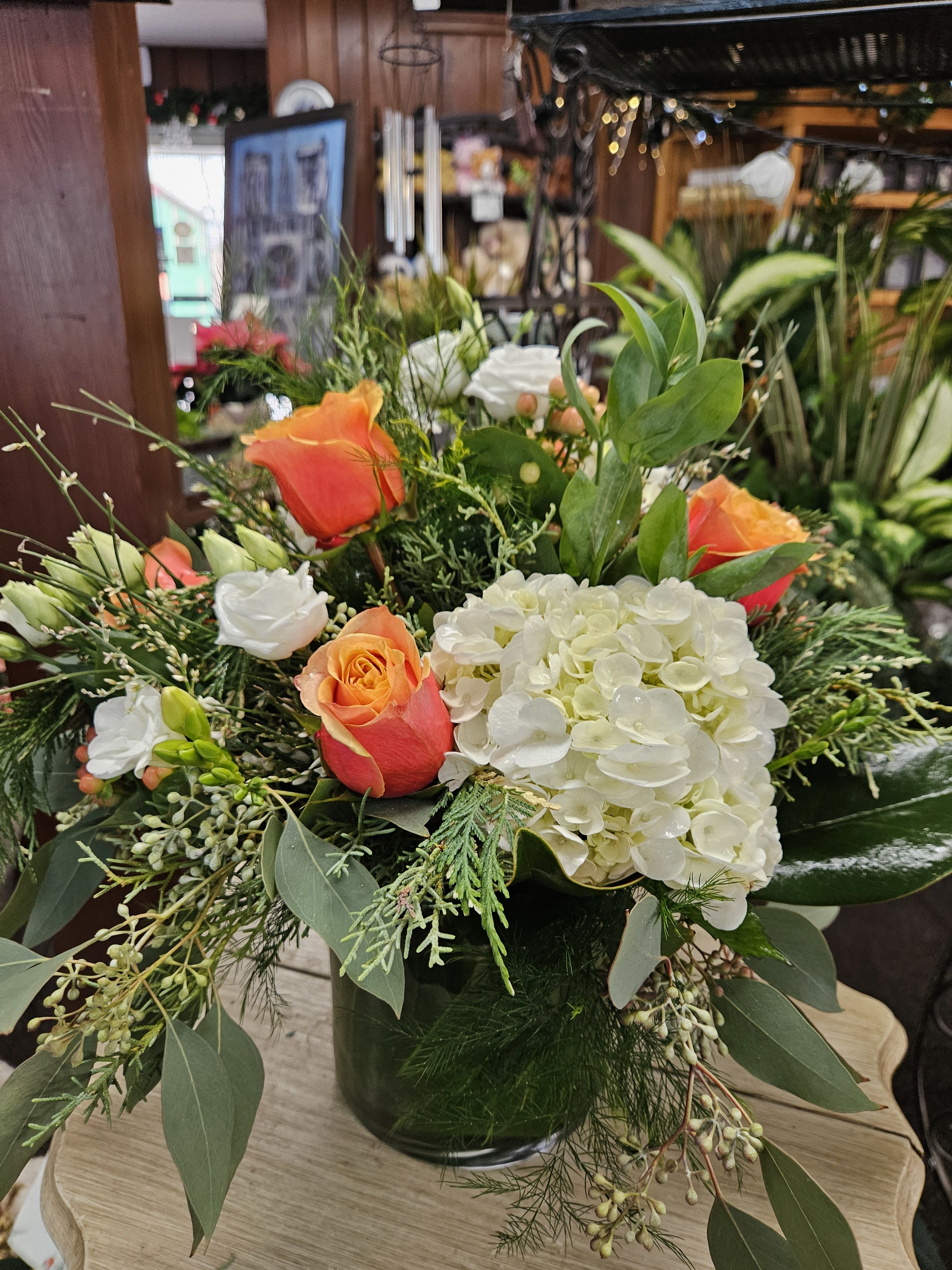 English Christmas Vase  - Unusual mix of Xmas greens, white hydrangeas, hypericum berries, mixed with Cherry Brandy roses, Lisianthus, Ginestra and Freesia in a cylinder low enough for a table . 