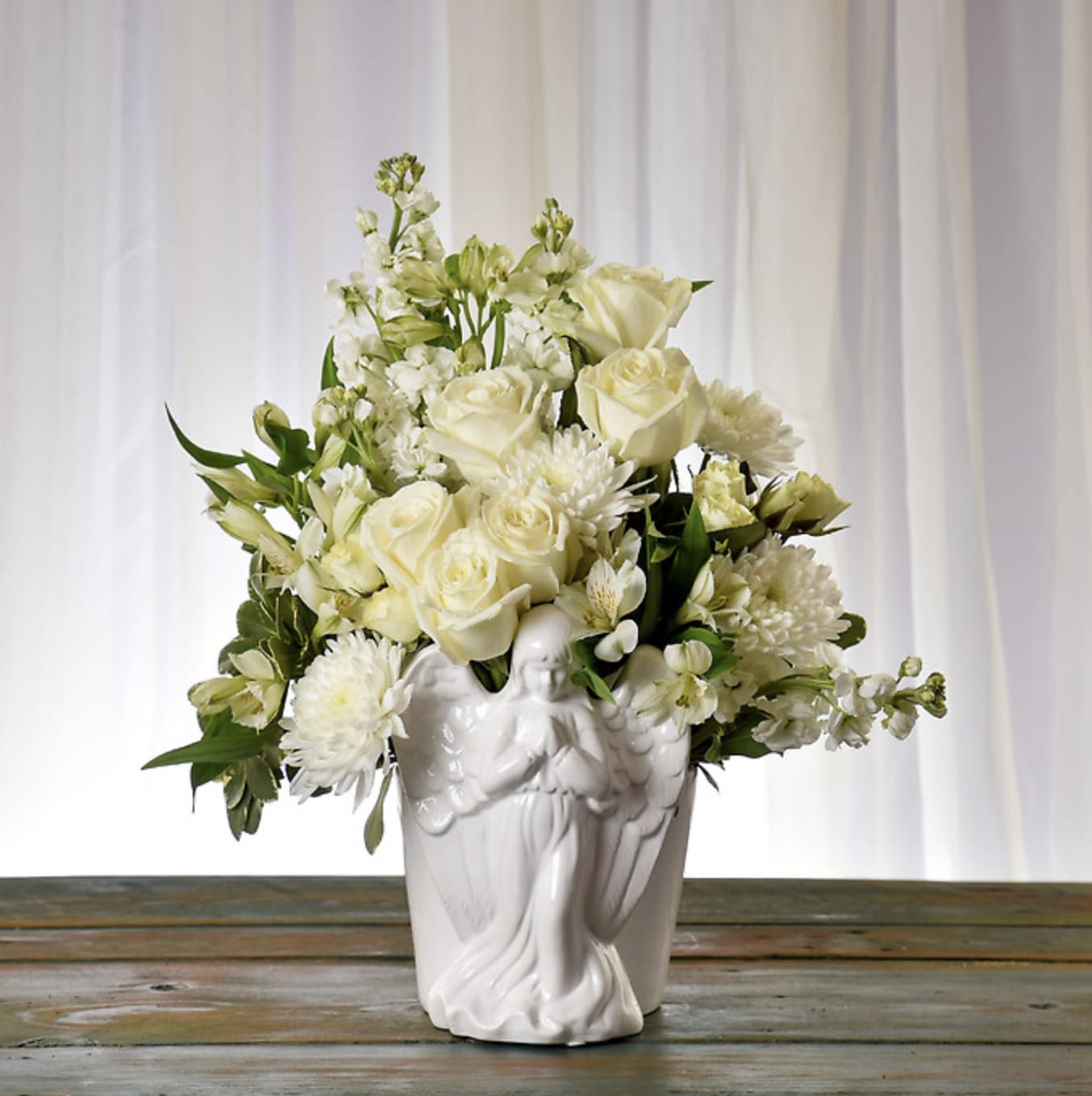 Heaven Sent - Presented in an elegant, ceramic angel vase, this assortment features white roses, white stock, white alstroemeria, and disbuds delicately arranged to wish your last goodbye. 