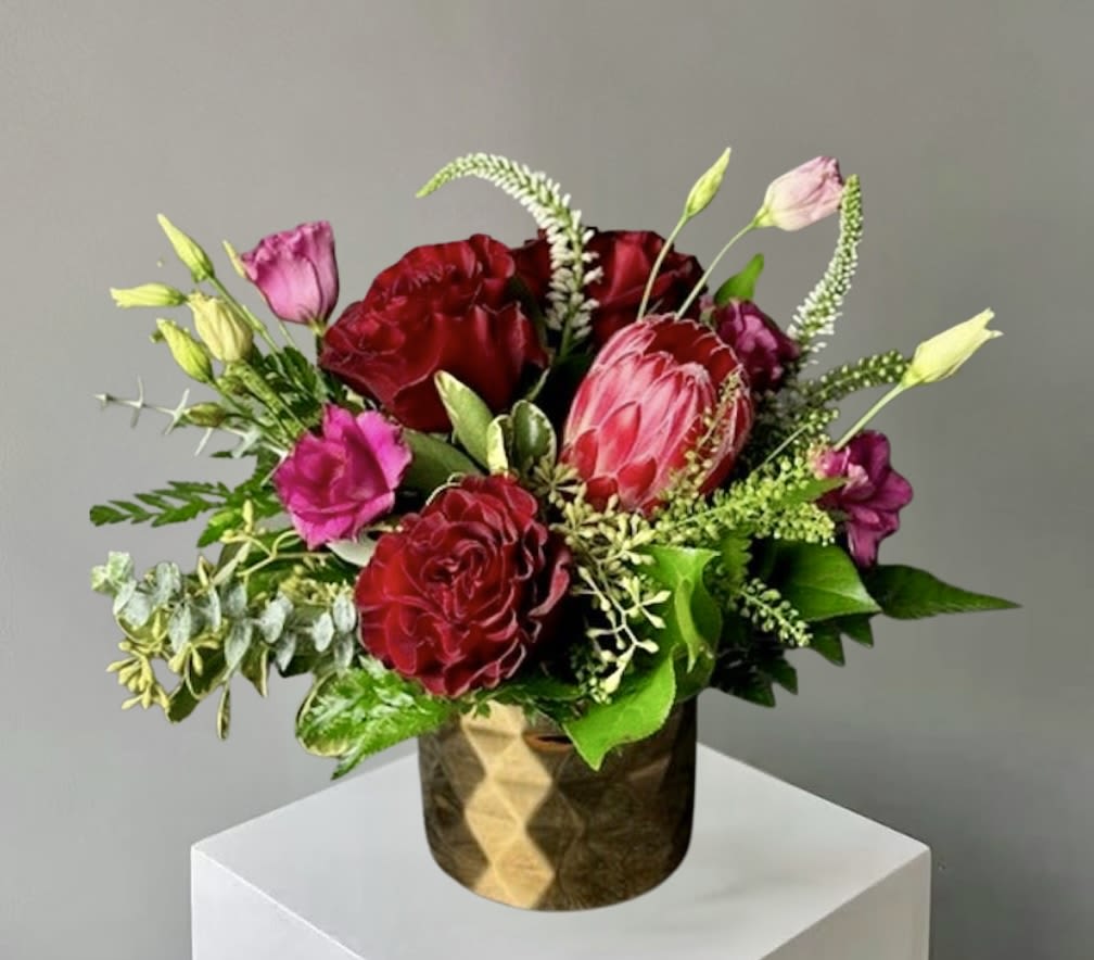 Yours Truly  - This striking floral arrangement features rich red roses beautifully paired with sculptural sugarbushes and an assortment of fresh, textured greenery. The deep, velvety red roses bring a sense of passion and elegance, while the unique sugarbushes add a bold, architectural element that gives the design a modern and distinctive character. Lush greens are thoughtfully woven throughout, creating depth, contrast, and a natural flow.