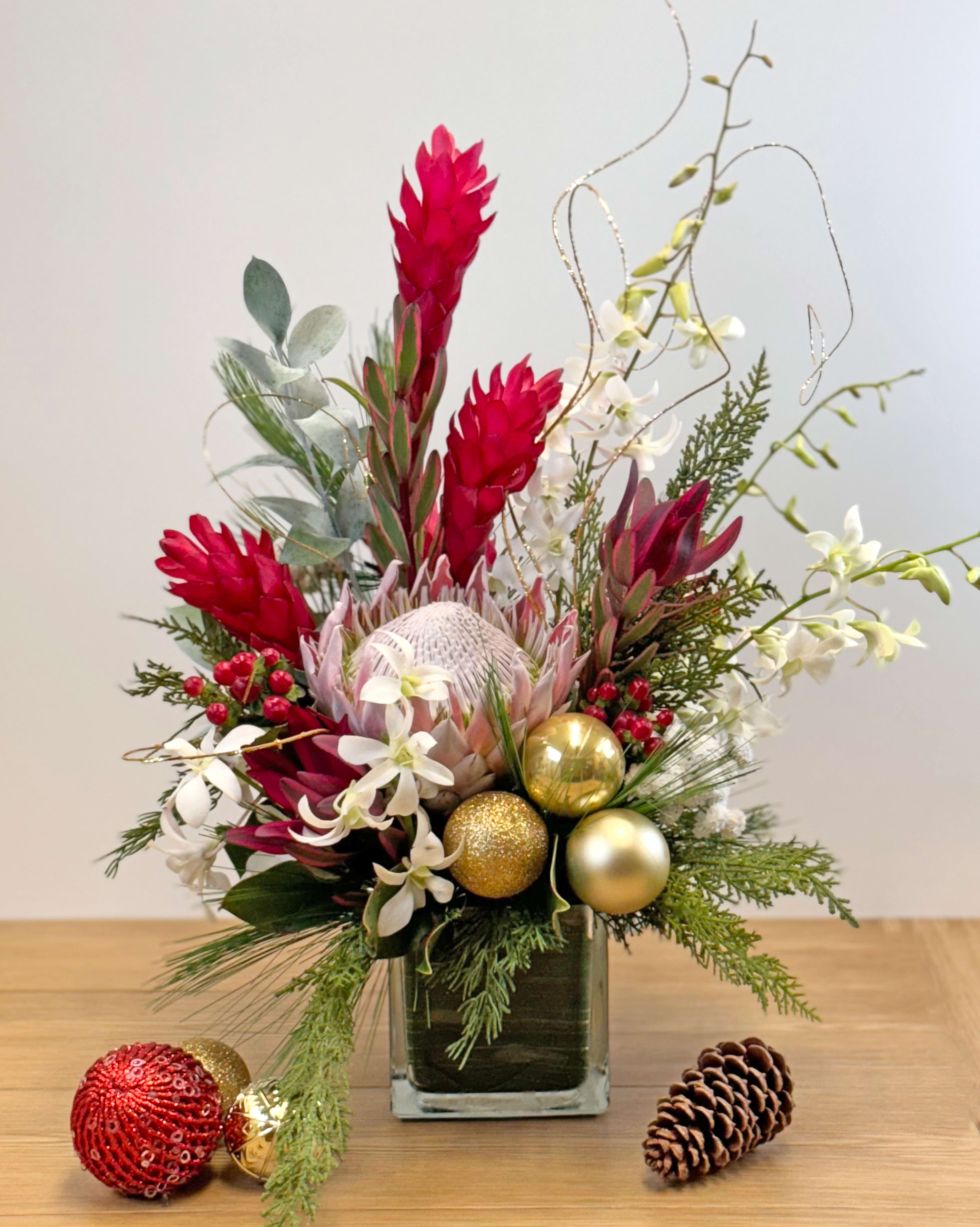 Christmas Magic in Hawaii (Sold out) - Contemporary Christmas Tropical Arrangement  Celebrate the holidays island style with our Contemporary Christmas Tropical Arrangement — a stunning fusion of locally grown tropical flowers and festive holiday charm, designed to bring warmth, color, and sophistication to any setting.  Featuring locally grown tropical blooms, this modern arrangement showcases the vibrant beauty of Hawaii with a unique twist on traditional Christmas décor.  Adorned with seasonal greens, pinecones, and festive ornaments, it beautifully blends tropical freshness with holiday cheer, creating a perfect balance of color and texture.  Modern Vase  Presented in a sleek, contemporary vase, this design complements both modern and classic interiors, making it a versatile piece that enhances any home or office.  Perfect for Any Space  Add a fresh and stylish holiday touch to your living room, office, or event space — perfect for creating a warm, welcoming atmosphere this Christmas season.  A thoughtful and uniquely Hawaiian holiday gift that combines the luxury of tropical flowers with the spirit of Christmas, perfect for clients, family, or friends.  Note: Christmas accessory on table not included.  Highlights   Locally grown tropical flowers   Accented with Christmas greens &amp; ornaments  