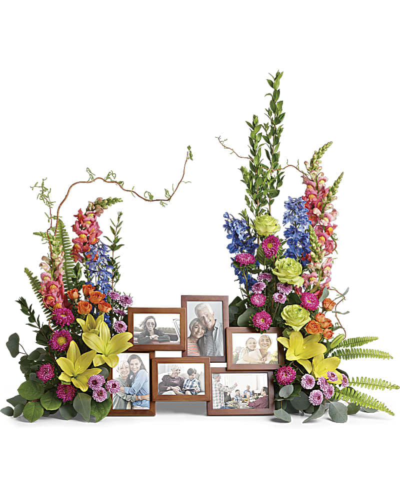 Loving Farewell Photo Tribute Bouquet - An awe-inspiring accent for your beloved photos at the service, this lush rose, lily and delphinium bouquet reflects a colorful life full of radiant memories. Green roses, orange spray roses, yellow asiatic lilies, blue delphinium, orange snapdragons, hot pink matsumoto asters, and lavender button spray chrysanthemums are accented with curly willow, myrtle, sword fern, silver dollar eucalyptus, and lemon leaf. Arrangement does not include picture frame.