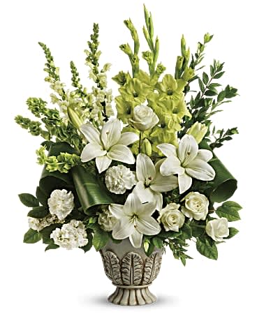 Clouds Of Heaven Bouquet - As serene as gently falling snow, this elegant white arrangement in a large antiqued pot is a heartfelt symbol of peace and beauty, a memory that will remain a guiding light to your loved ones for years to come. White roses, white asiatic lilies, green gladioli, white carnations, bells of ireland, white snapdragons, and white stock are accented with myrtle, green ti leaves, and lemon leaf.