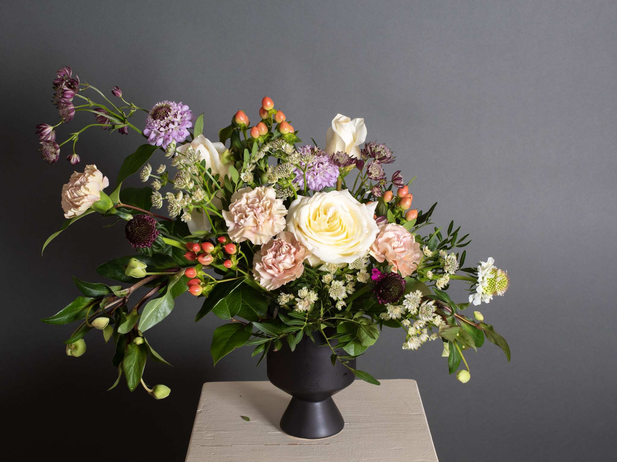 Florence, Wanderlust series - Ceramic Pot Arrangement - Our garden inspired arrangement is comprised of the seasons best blooms. Roses, carnations, hypericum berries, scabiosas and seasonal foliage in a soft neutral colour palette contrasted with the black ceramic de ville pot.  Product shown at $134.95  Pot size : 4.5in X 6.25in