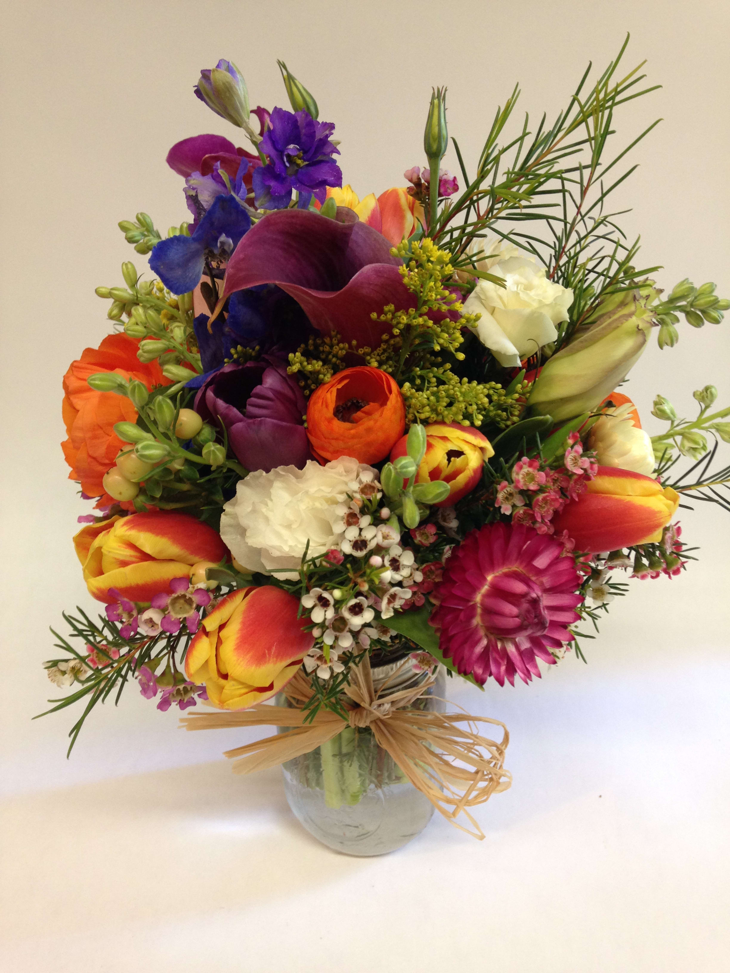 Sweet and Seductive Premium Garden Jar - FVSF - A joyful explosion of color and charm, the Sweet and Seductive  Bouquet is the perfect pick-me-up for any occasion. Featuring a radiant mix of tulips, calla lilies, carnations, green dianthus, spray roses, stock,  blue Bella Donna, and wax flowers, this arrangement brings together shades of orange, purple, yellow, and magenta with rustic greenery and wildflower texture.    Finished with a natural twine bow and arranged in a clear glass jar, it's ideal for birthdays, get-well wishes, or simply bringing the sunshine indoors.    Note: Each bouquet is unique—flower varieties may vary seasonally while keeping the overall look bright    . (Some flowers may be subject to change depending on the season. We will contact you with available flower substitutions; please contact us with specific questions if you are concerned with flower availability, thanks!)  Featured arrangement: $78.75 (Regular Price)