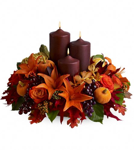 Center of Attention  - The centerpiece on your holiday table this year should be bright, decorative and eye-catching - and this lovely display of fresh fall blossoms such as Asiatic lilies, orchids and roses, accented with faux grapes and pumpkins, is simply perfect! Three chocolate-colored pillar candles complete the tableau.    A mix of fresh flowers such as roses, orchids, Asiatic lilies and a chrysanthemum, in shades of bronze and orange - accented with seeded eucalyptus, preserved oak leaves and faux grapes and pumpkins - is arranged in a tray around three chocolate-colored pillar candles of different heights.    Approximately 18" (W) x 13" (H)    Orientation: All-Around        As Shown : TFWEB444    