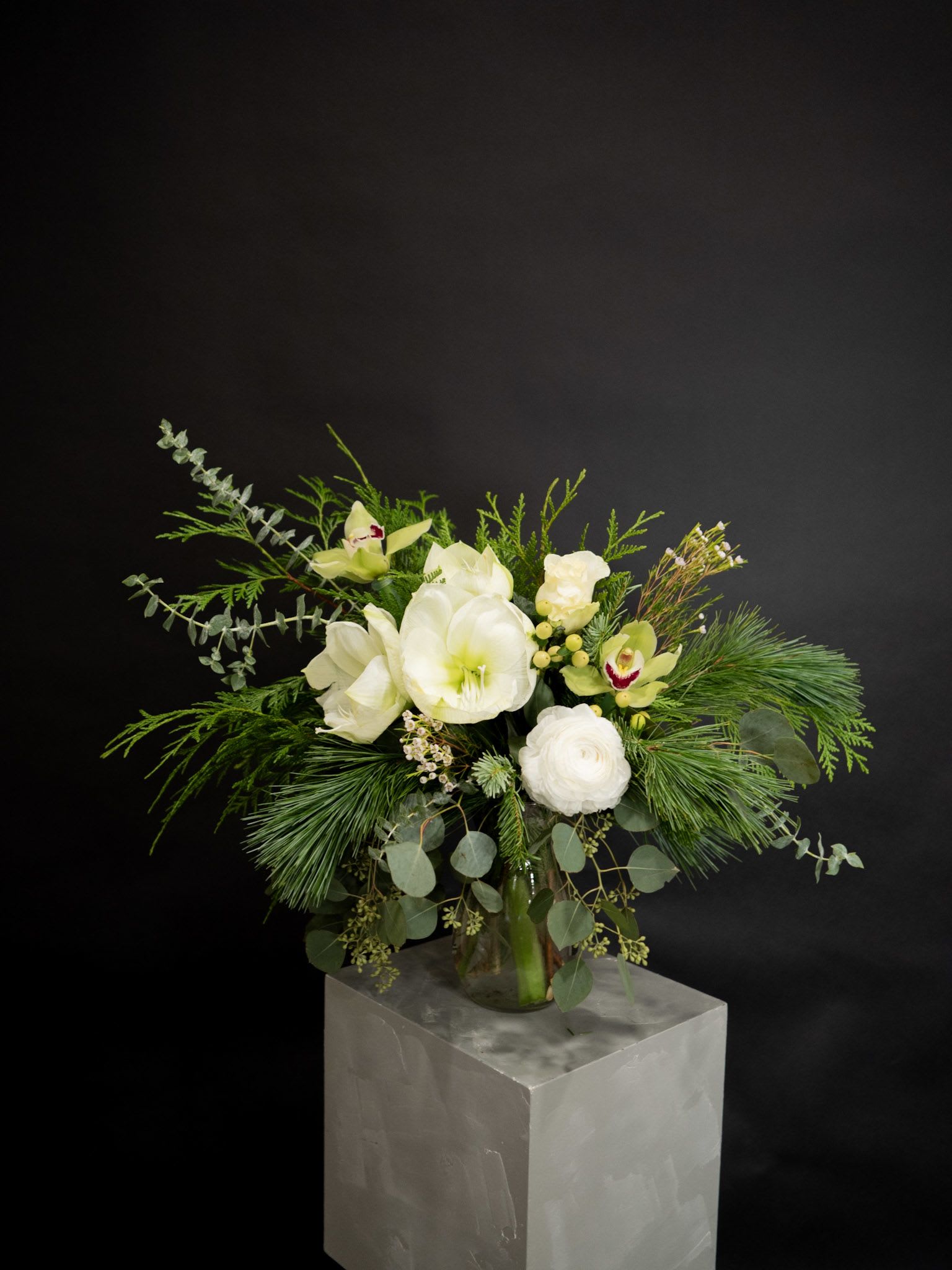 Snowflake Vase Arrangement - This elegant winter arrangement captures the serene beauty of a snow-dusted landscape. Featuring lush white blooms such as amaryllis, ranunculus, and cymbidium orchids, accented with wax flowers, eucalyptus, pine, and other seasonal greenery, this design brings the calm and crispness of winter into your home. Perfect for celebrating the holidays or adding a touch of sophisticated charm to any winter occasion.
