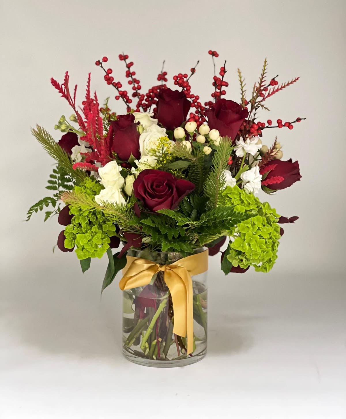 Evening Harmony - This elegant floral arrangement features rich red roses, soft white blooms, seasonal greenery, and textured berry accents, thoughtfully designed in a clear glass vase and finished with a refined gold ribbon. Balanced and timeless, it brings warmth and sophistication to any Holiday table or living space, making it an ideal gift especially for Shabbat dinners, meaningful celebrations, or simply to express appreciation with style and grace.
