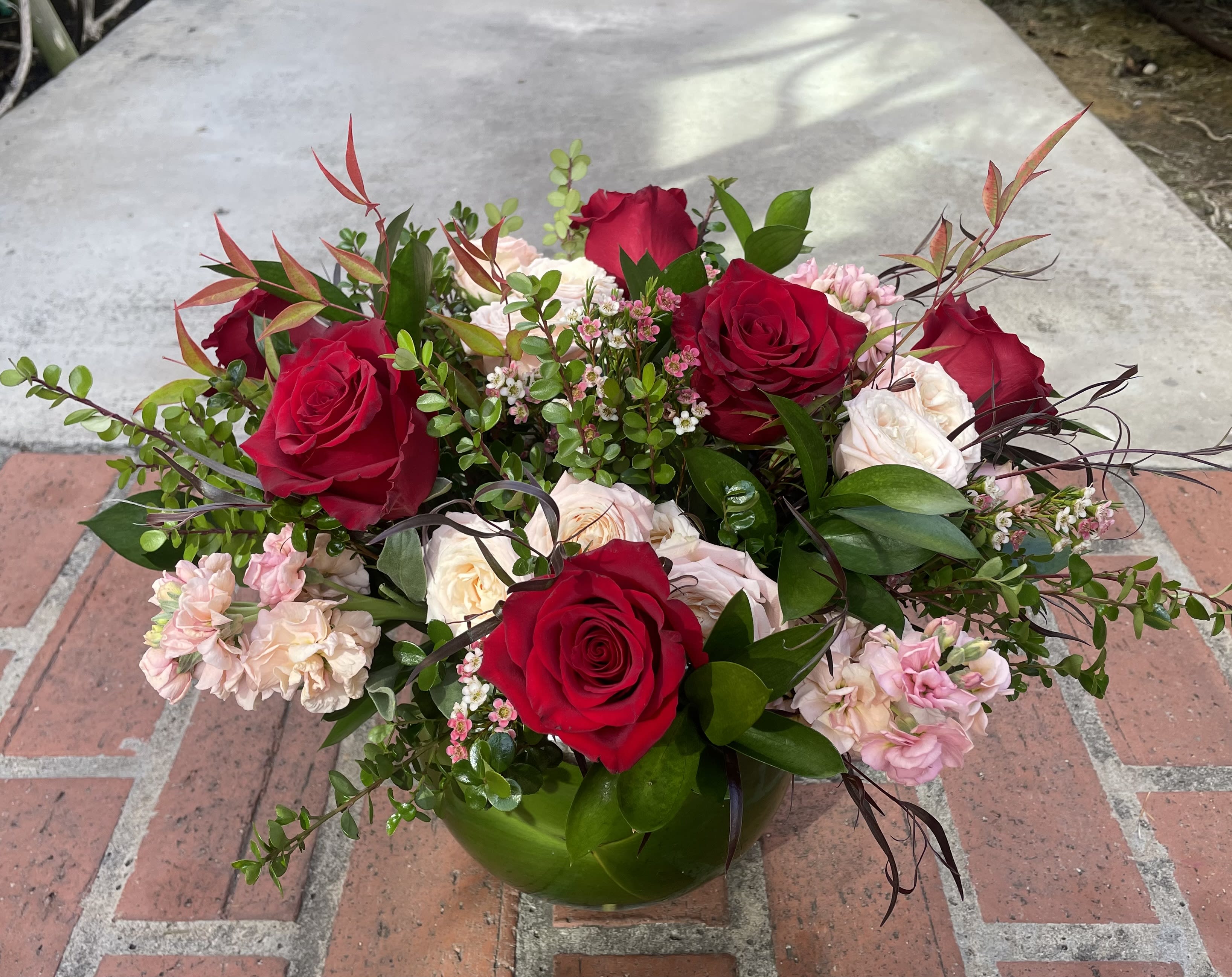 Lovely Mix - A lovely bowl filled with a half dozen red roses mixed with other fresh blooms in romantic shades of pink, peach and red. 