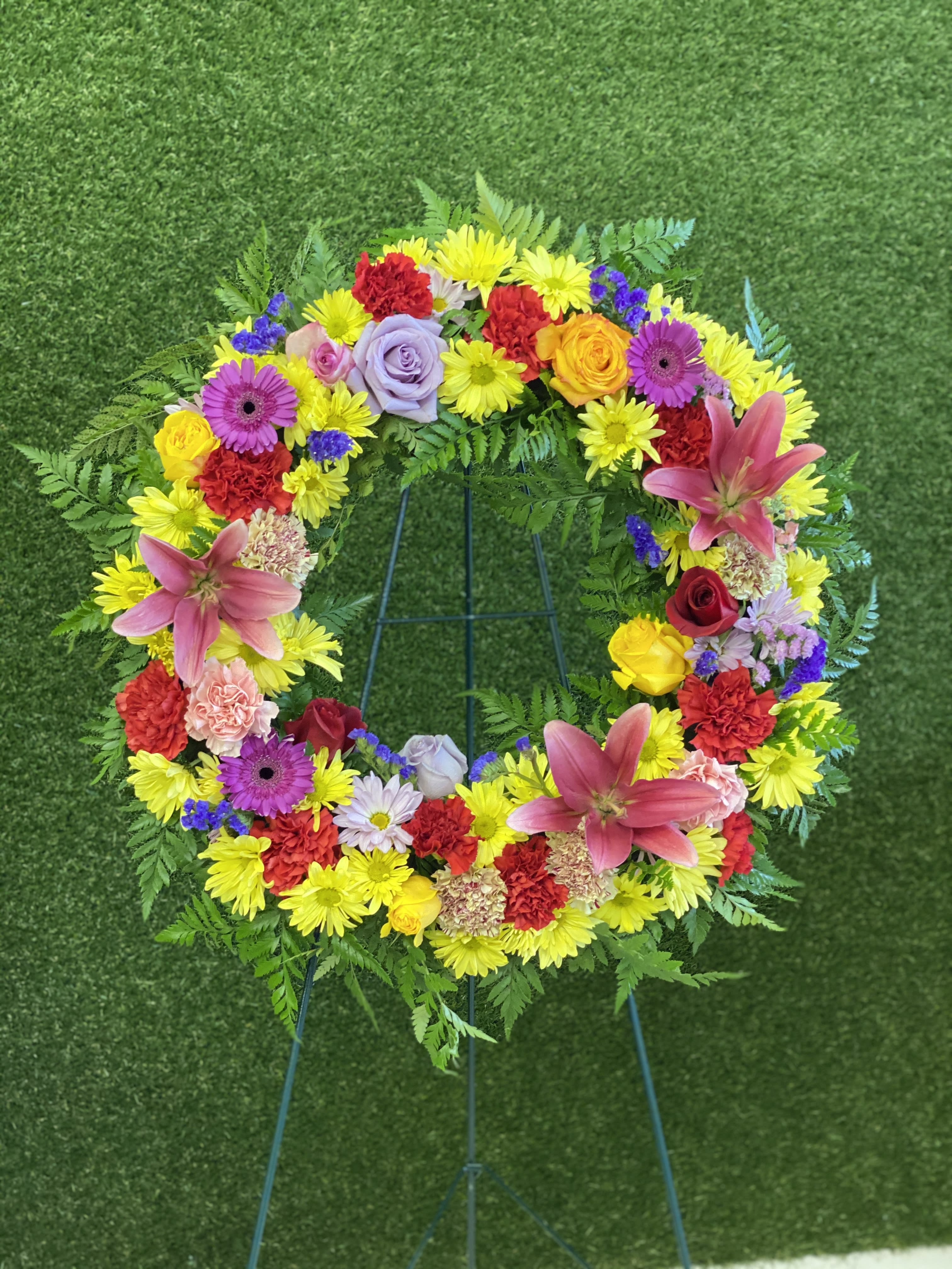 COLORFUL SERENETY - This Standing Wreath is a beautiful reflection of your love and sympathy. Colorful flowers such as roses,carnations, daisies, lilies, assorted premium flowers and greenery. Sent directly to the funeral home by family, friends and business associates, colors and assortment may vary while keeping the same look and feel.  STANDARD: THREE DOZEN ROSES DELUXE: FOUR DOZEN ROSES PREMIUM: 5 DOZEN ROSES  Picture is a DELUXE.  INCLUDES A COMPLIMENTARY golden card with envelope, please send card message with the order.