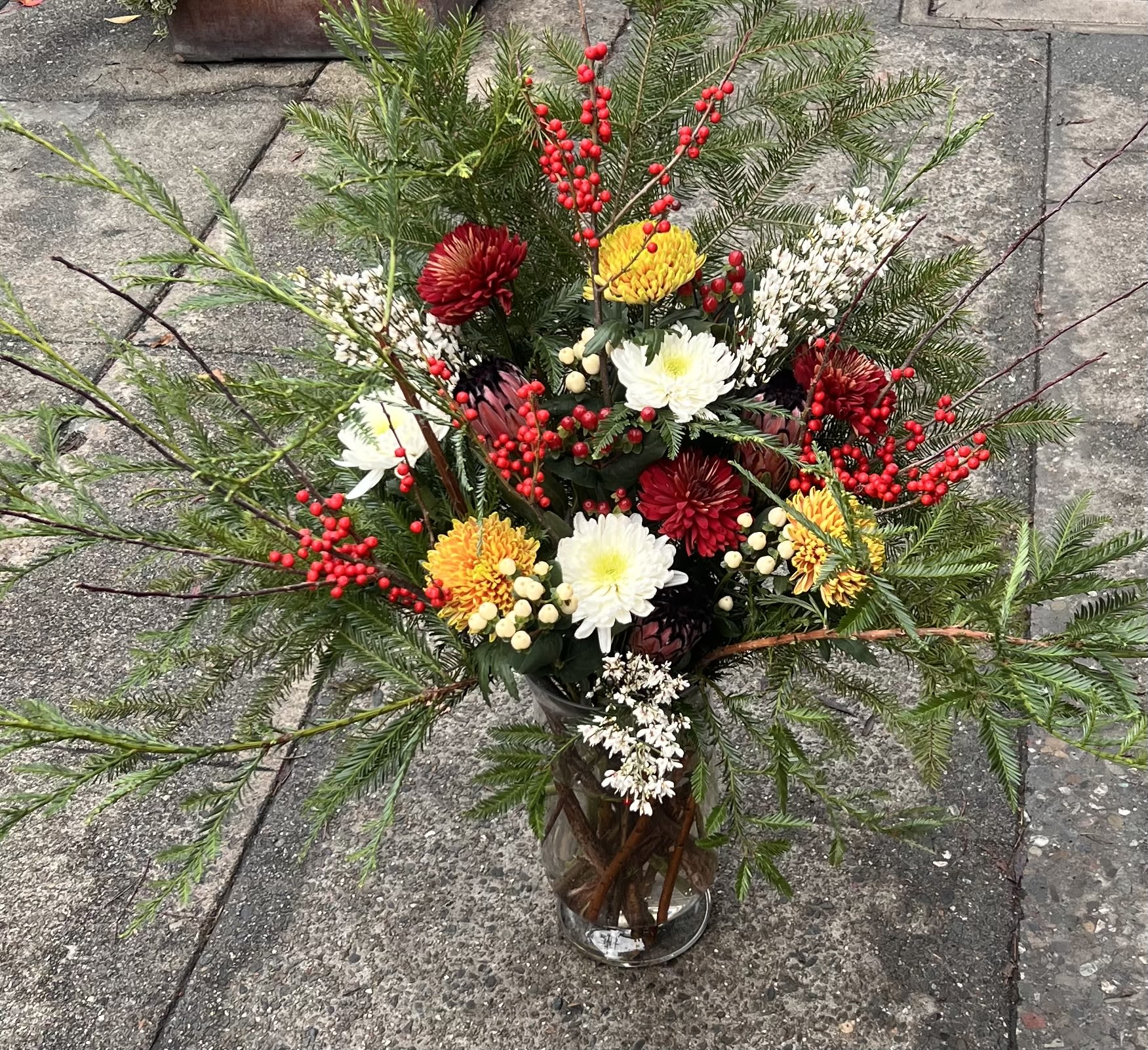 Winter Festive  - An artistic woodland composition featuring cedar greens, crimson berries, and sculptural blooms in ivory, burgundy, and gold. Winter Forest Sonata evokes the stillness of a snow-kissed forest — elegant, textural, and full of holiday magic. Designed for statement moments, grand entrances, and homes that celebrate the season with style. 