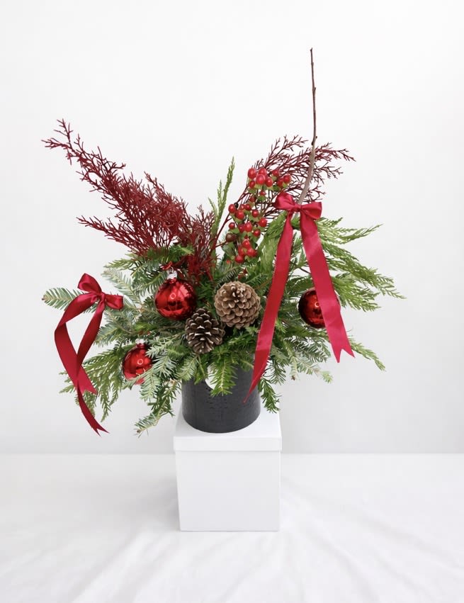 Christmas  Gift Arrangement - Celebrate the holiday season with our Holiday Evergreen Floral Arrangement, a luxurious Christmas greenery design made with fresh seasonal evergreens, pine branches, natural pinecones, festive red ornaments, winter berries, and elegant red satin ribbons.  This handcrafted Christmas floral arrangement is beautifully designed in a modern black container and makes the perfect holiday gift box, Christmas centerpiece, or festive home décor piece. Ideal for gifting, hosting, or adding warmth and elegance to any space during the holidays.  Each arrangement is made fresh to order using premium holiday greenery, ensuring a unique and high-quality seasonal design.  christmas flowers in myrtle beach