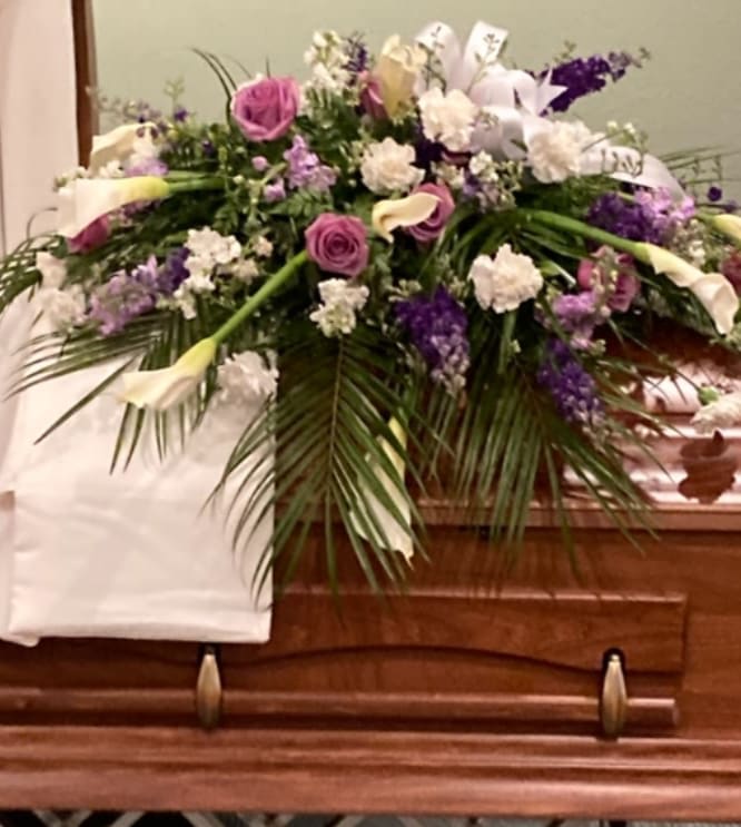 CASKET SPRAY FLOWERS - PURPE LOVE - PURPLE AND WHITE FLOWERS, AND ASSORTED GREENS ADORN THE CASKET. 